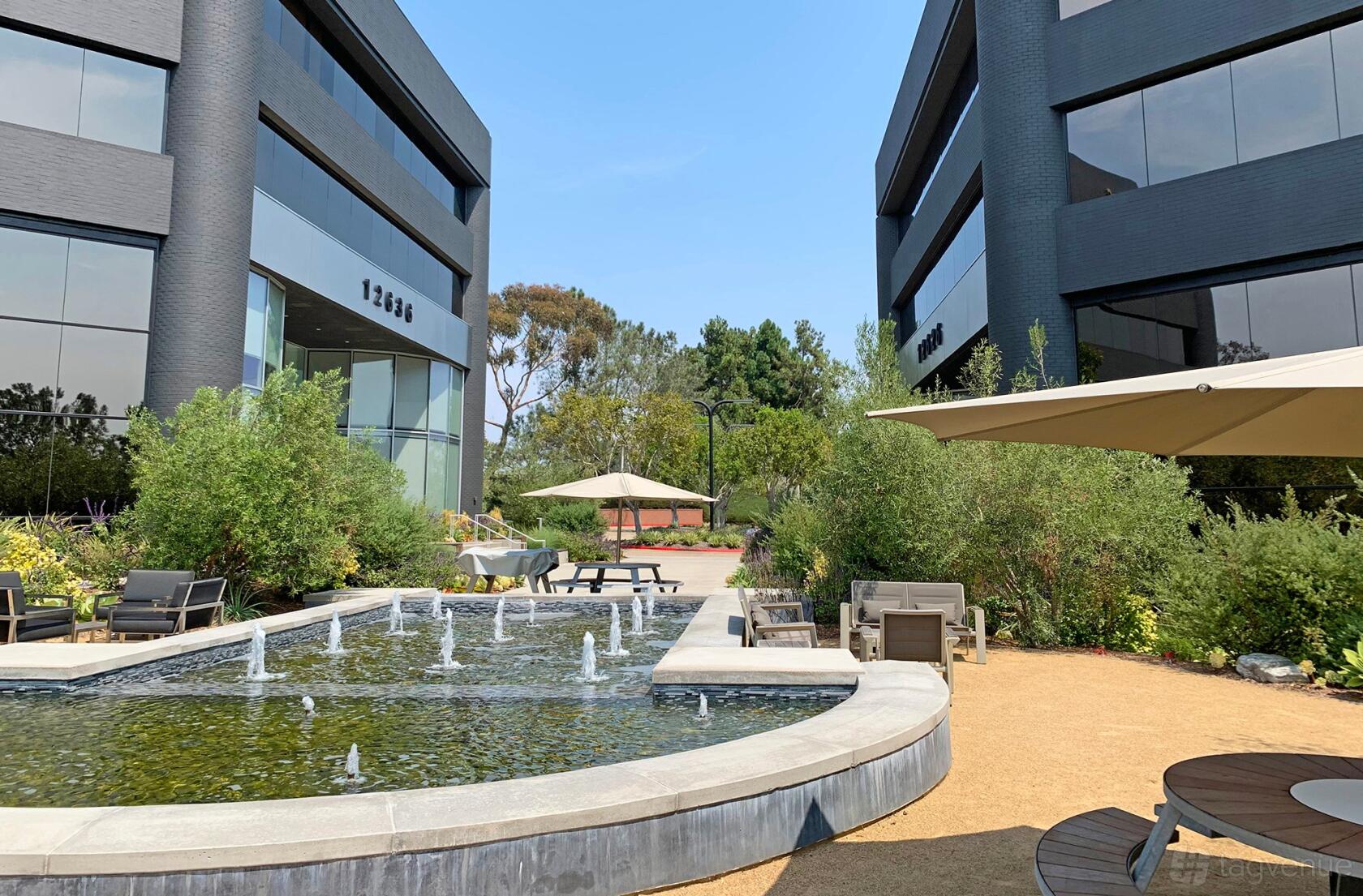 A meeting centre with a courtyard featuring a rectangular water fountain, patio seating, and umbrellas at Premier Workspaces - Del Mar Corporate Plaza.