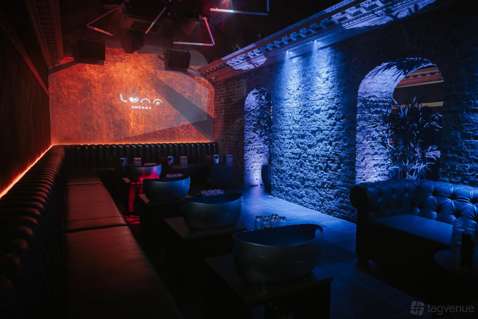 A restaurant lounge with exposed brick walls, colorful accent lighting, and leather sofas at Inca London.