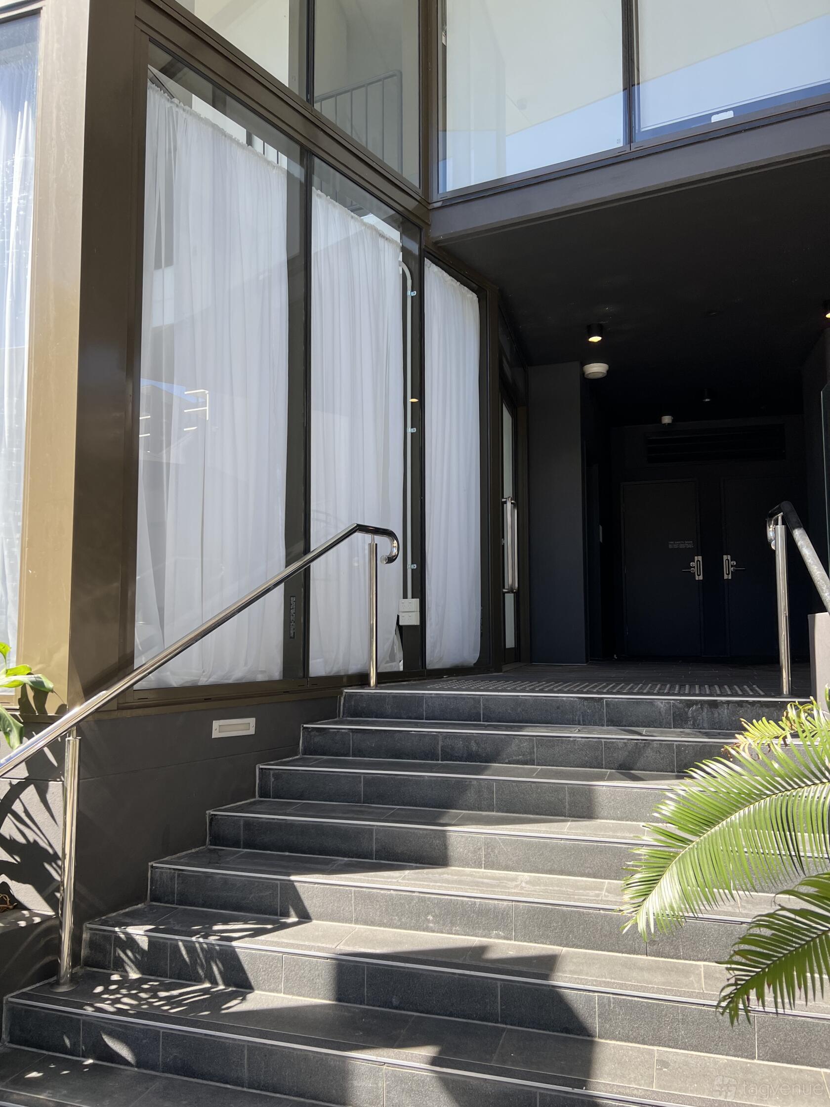An entryway with glass doors, floor-to-ceiling white curtains, and a black tiled staircase at 1124 The Studio.