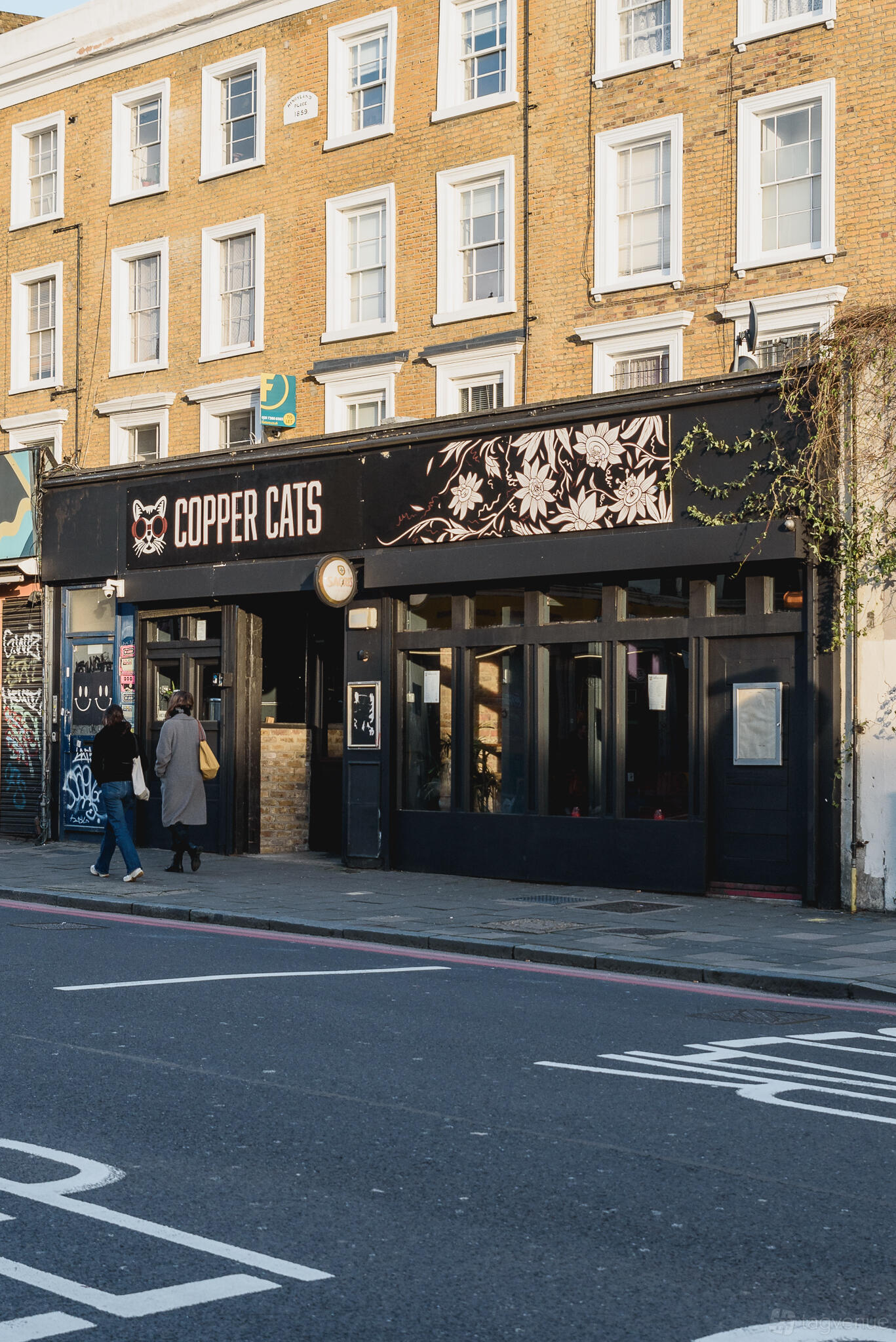 A pub with a black exterior, large front windows, floral signage, and a small entrance at Copper Cats.