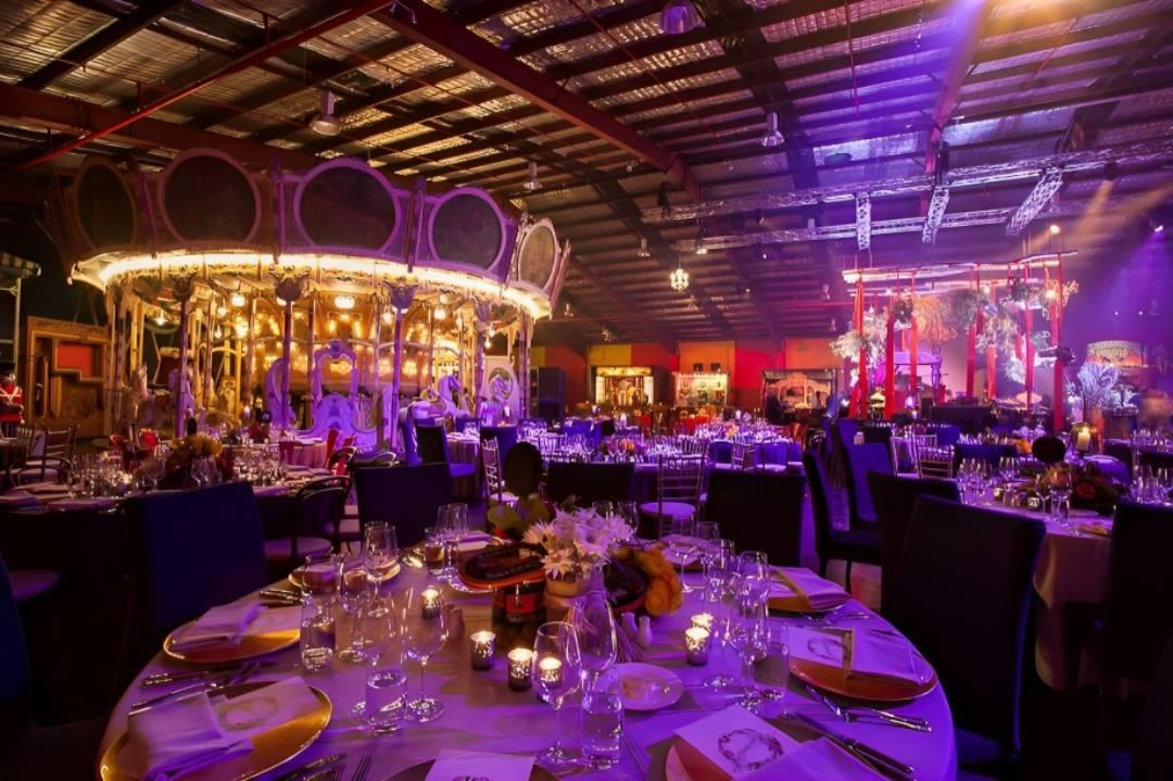 An event venue with carousel, round tables set with glassware, and stage lighting at Fairground Follies.