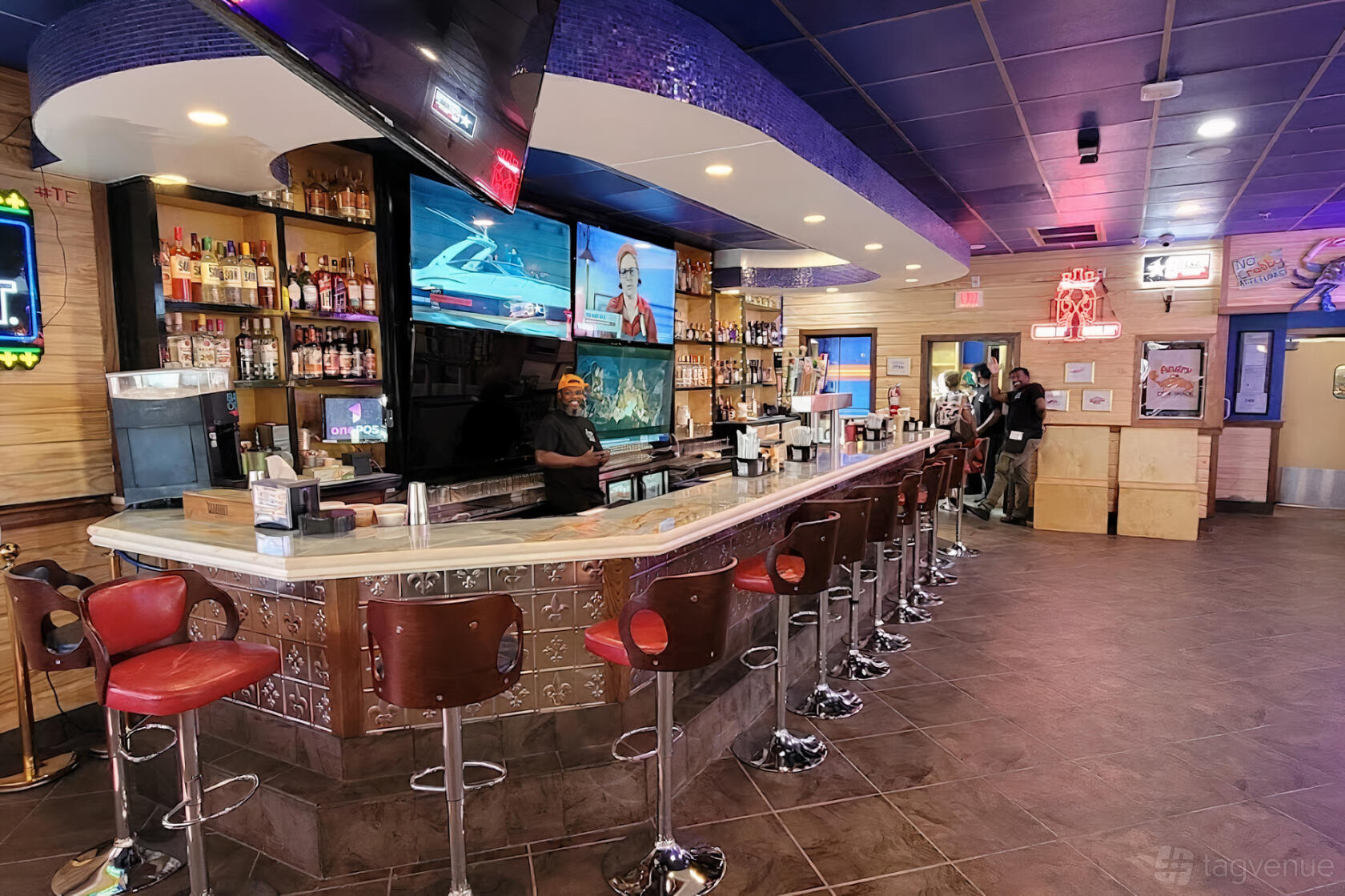 A restaurant with a long bar, red barstools, liquor shelves, and multiple TVs at Angry Crab Shack.