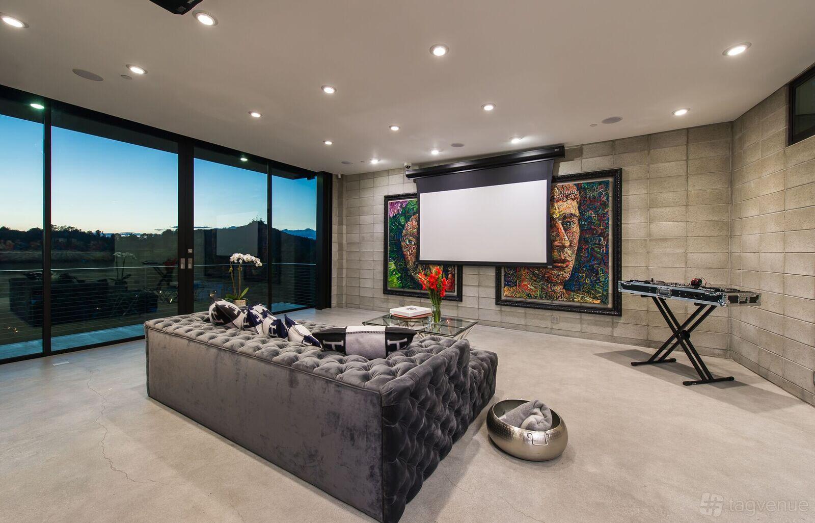 An event venue with a plush gray sofa, projection screen, concrete floors, and large windows at The Glass Mansion.