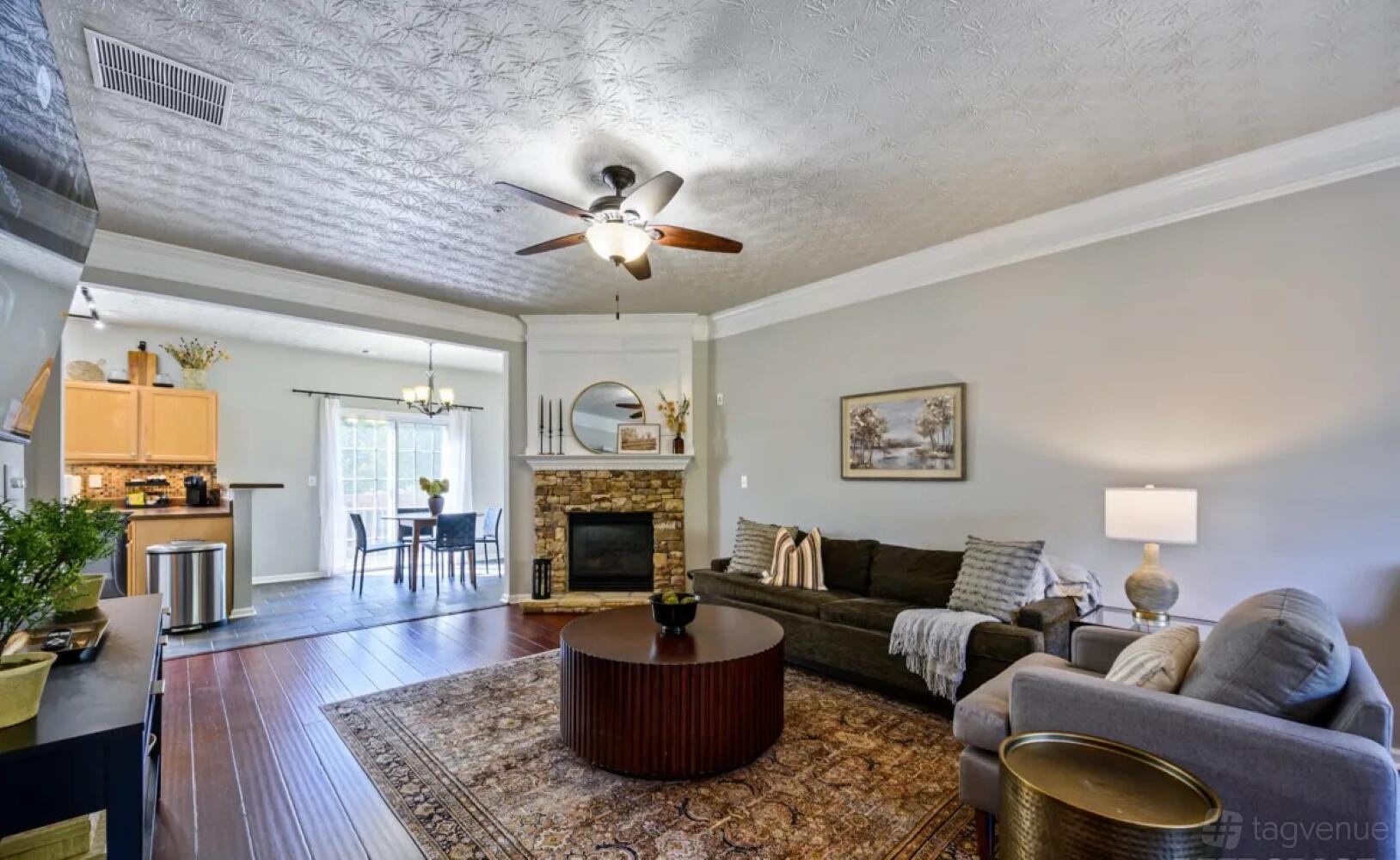 A living room with a stone fireplace, ceiling fan, and wood floors at Suite Stays Atlanta - Bay Overlook, Woodstock.