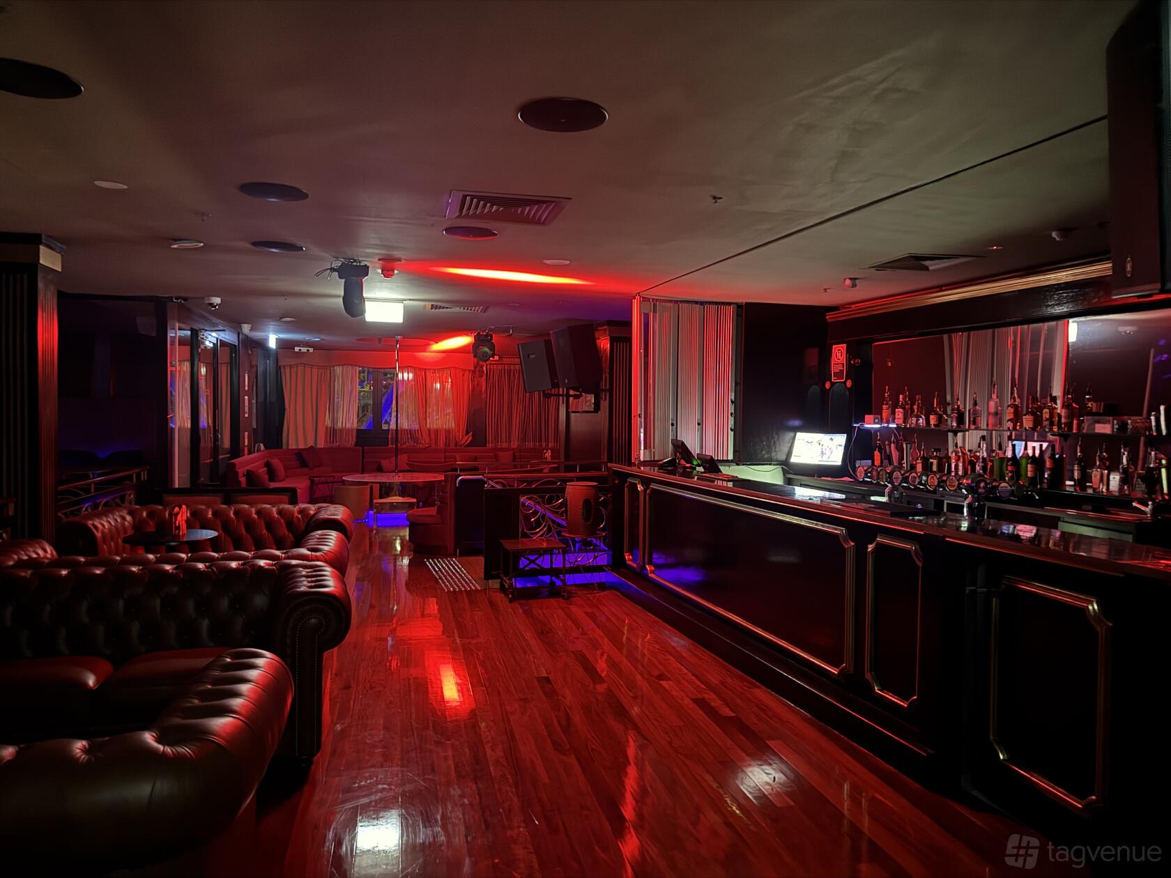 A nightclub with red mood lighting, leather sofas, and a long mirrored bar at Sydney Elements.