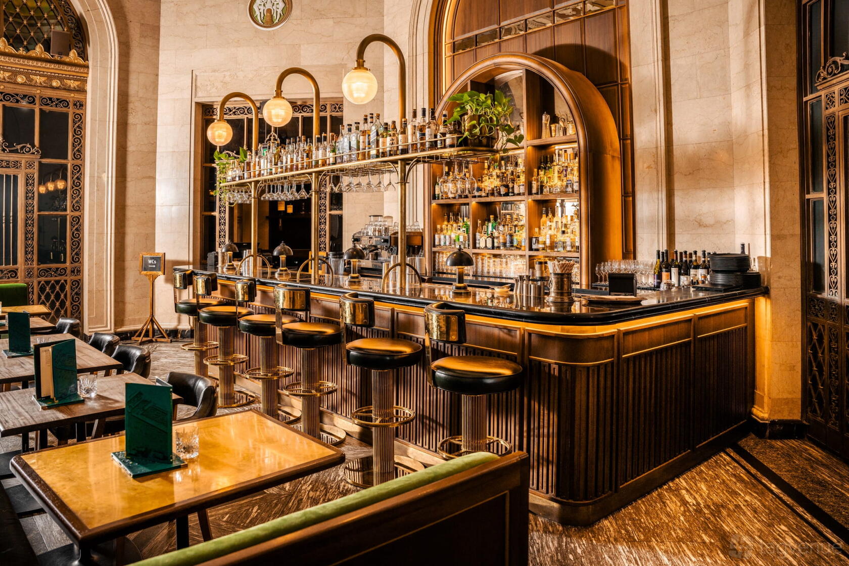A cocktail bar with a marble countertop, vintage bar stools, globe pendant lights, and arched shelving at Hawksmoor Liverpool.