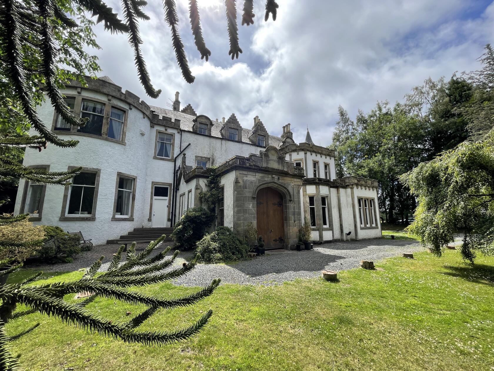 A country house with arched stone entryway, large bay windows, and surrounded by trees at Harvieston Hall.