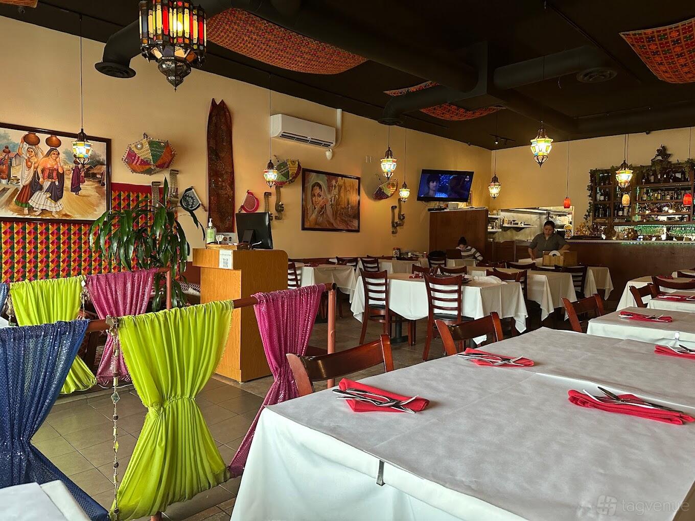 A restaurant with colorful drapes, white tablecloths, hanging lanterns, and traditional artwork at All India Cafe - Glendale.