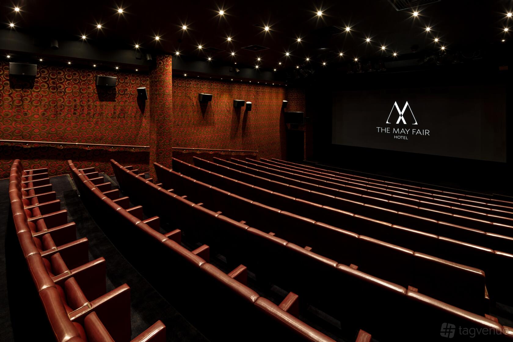 An auditorium-style hotel theatre with leather seats, patterned walls, and a large projection screen at The May Fair Hotel.