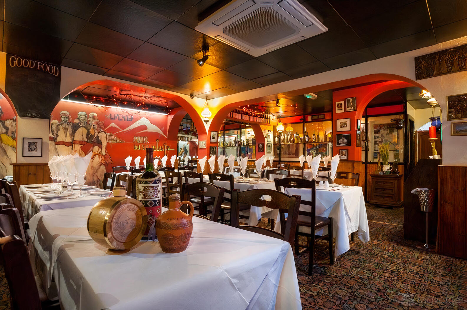 A restaurant with arched doorways, colorful murals, and tables set with white linens at Armenian Taverna.