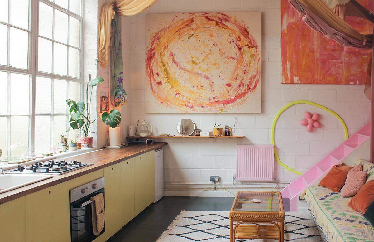 An art studio with tall factory windows, abstract wall art, and a pastel kitchen at Colour Design Studio.