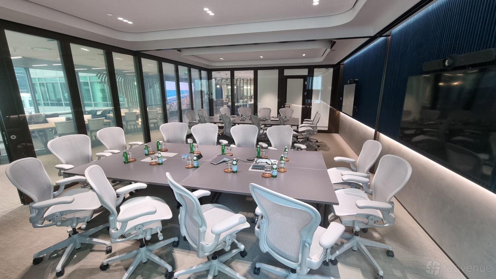 A meeting room with modular tables, ergonomic chairs, glass walls, and bottled water at Capital Square.