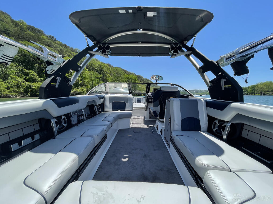 A boat with wraparound cushioned seating, open deck, and sunshade on the water at Good Vibes Boat Rental Lake Travis.