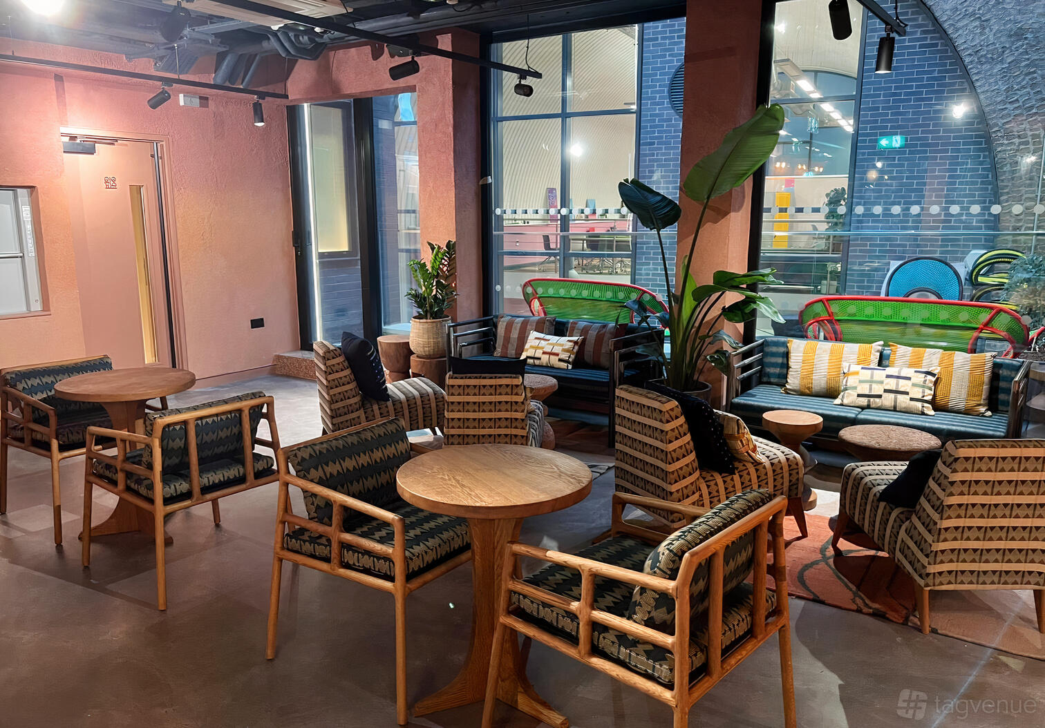 A lounge with patterned armchairs, round wooden tables, and colorful sofas near large windows at The Africa Centre.