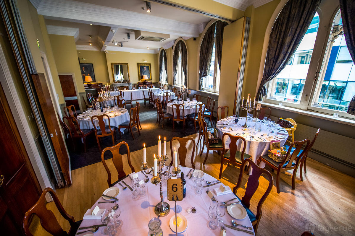 An event space with round tables set with candelabras, wooden chairs, and large arched windows at Racquet Club Hotel & Ziba Restaurant.