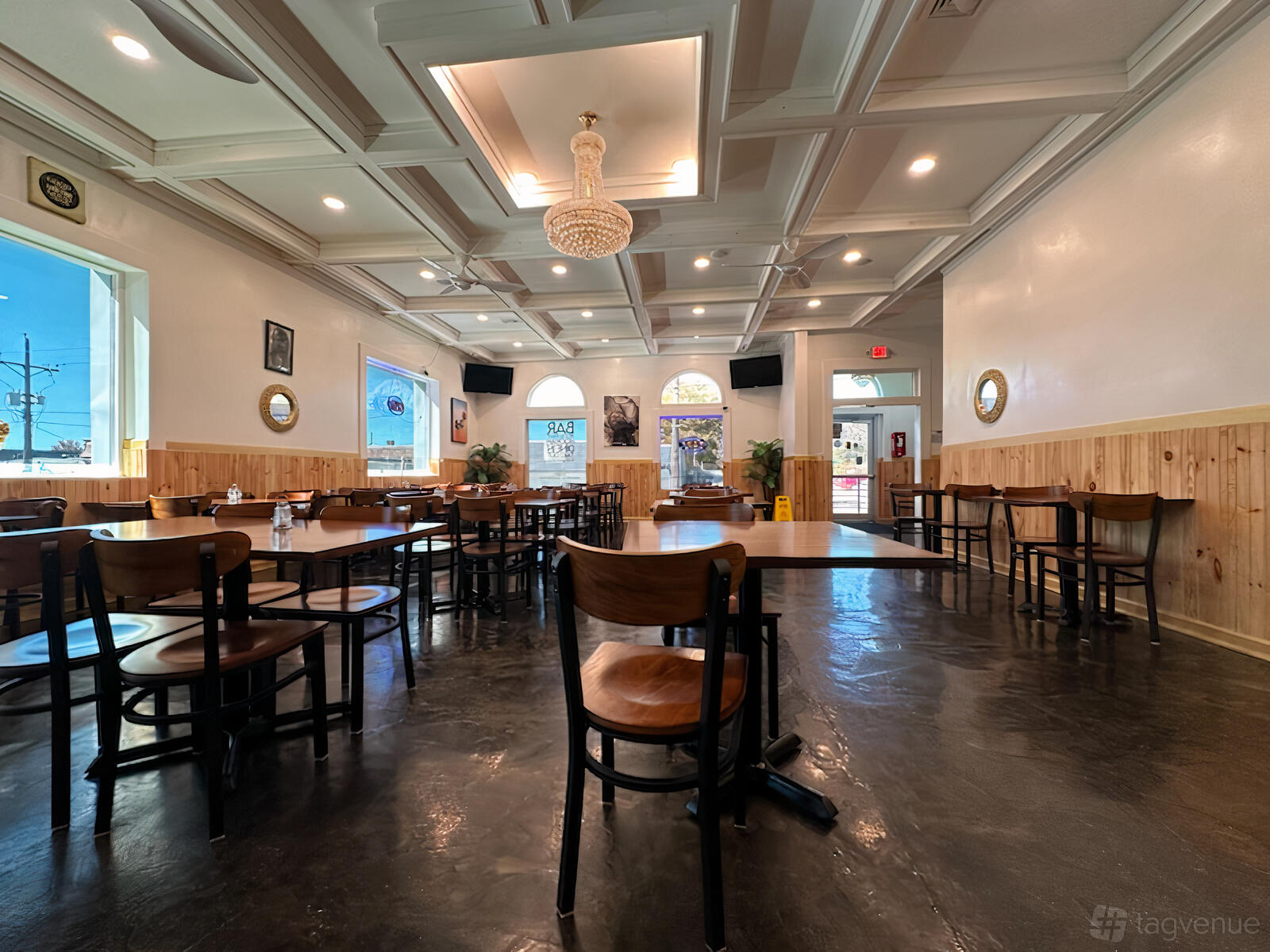A restaurant dining area with wooden chairs, square tables, a chandelier, and large arched windows at K & R International Restaurant & Bar.