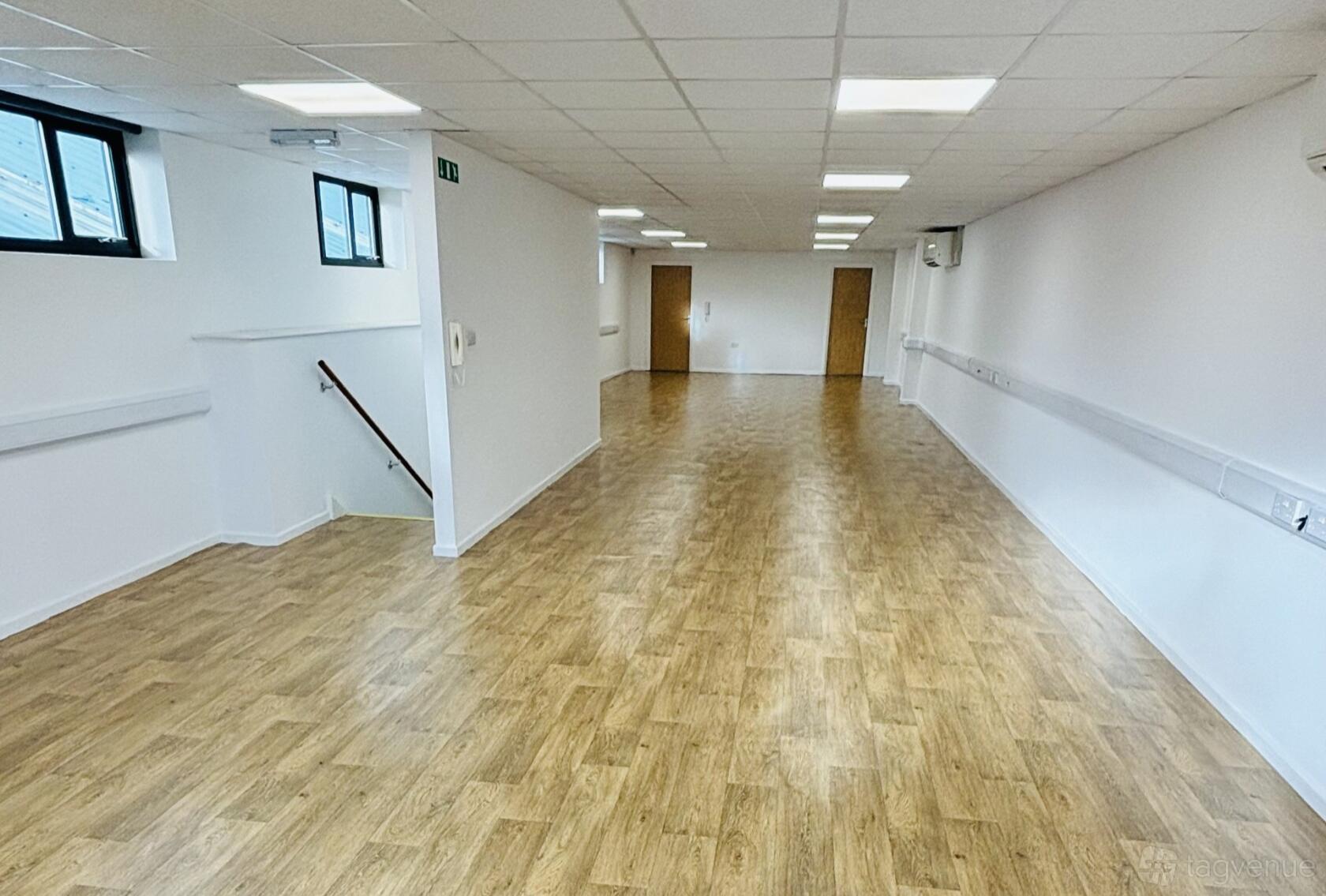 An event space with wood flooring, white walls, overhead fluorescent lighting, and windows at Unity Studios BS2.