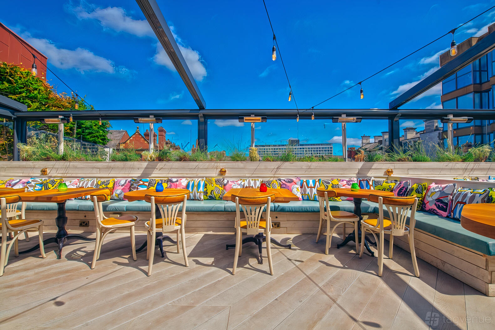A restaurant terrace with colorful patterned bench seating, round wooden tables, and string lights at Revolucion de Cuba Newcastle.