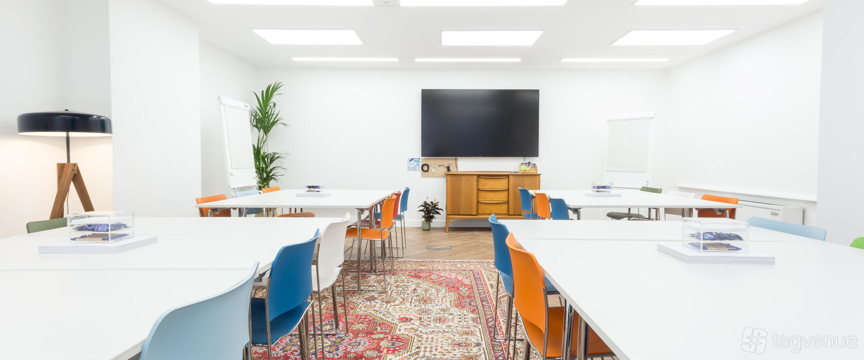 An event venue with white walls, colorful chairs, a large screen, and a patterned rug at Wallacespace Covent Garden - 53 Parker Street.