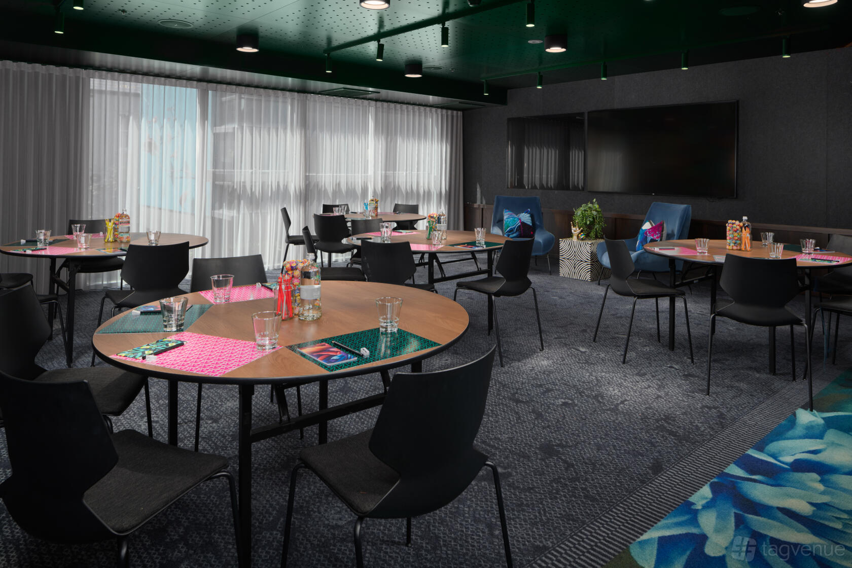 An event space with round tables, black chairs, floor-to-ceiling windows, and a large TV screen at Zagame's House.