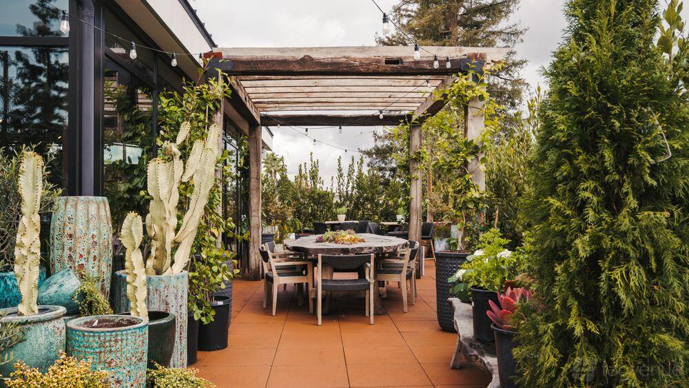 An outdoor patio with a wooden pergola, potted plants, and a long dining table at Rolling Greens - Studio City Location.