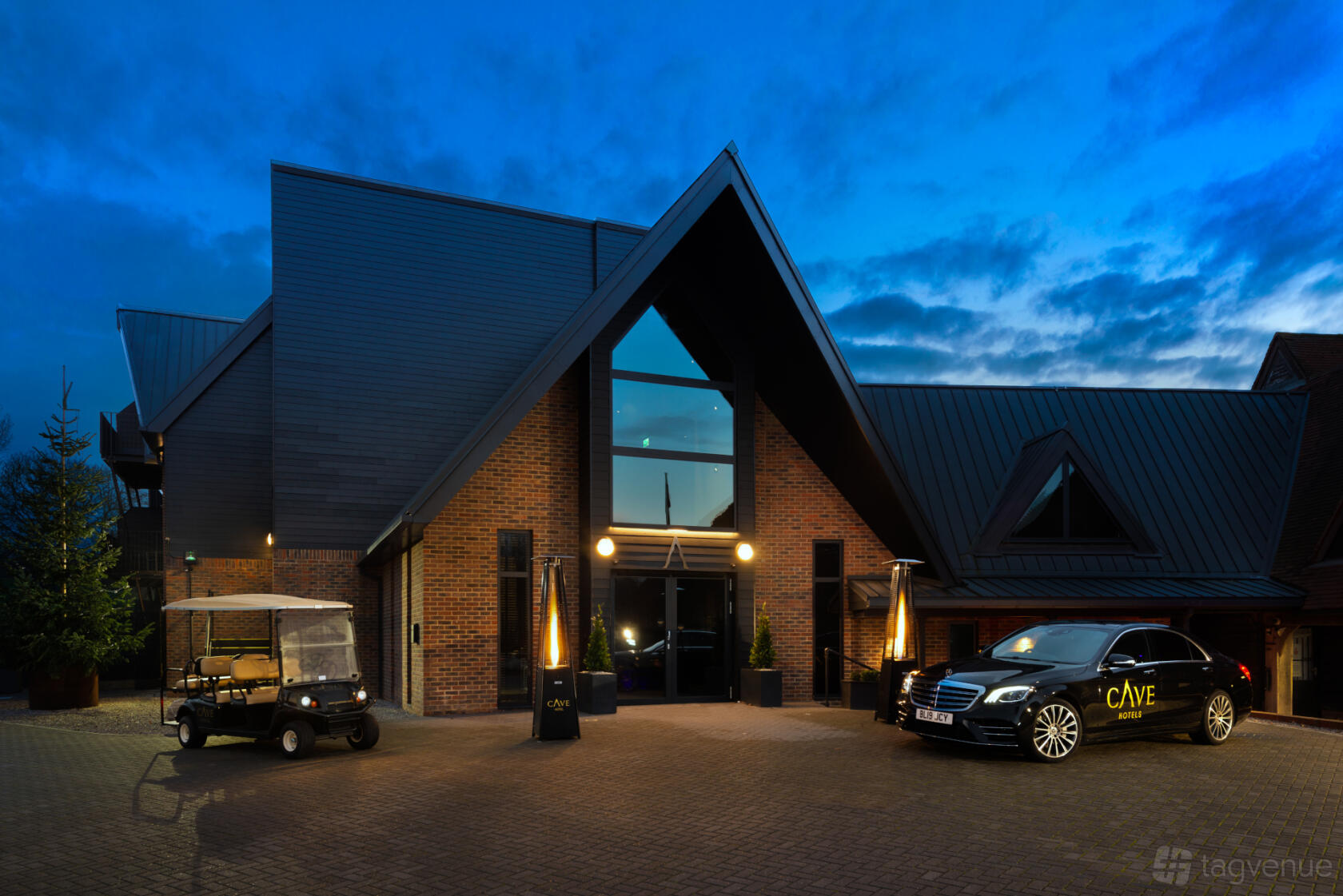 A hotel entrance with modern peaked roofs, brick facade, and parked vehicles at Cave Hotels.