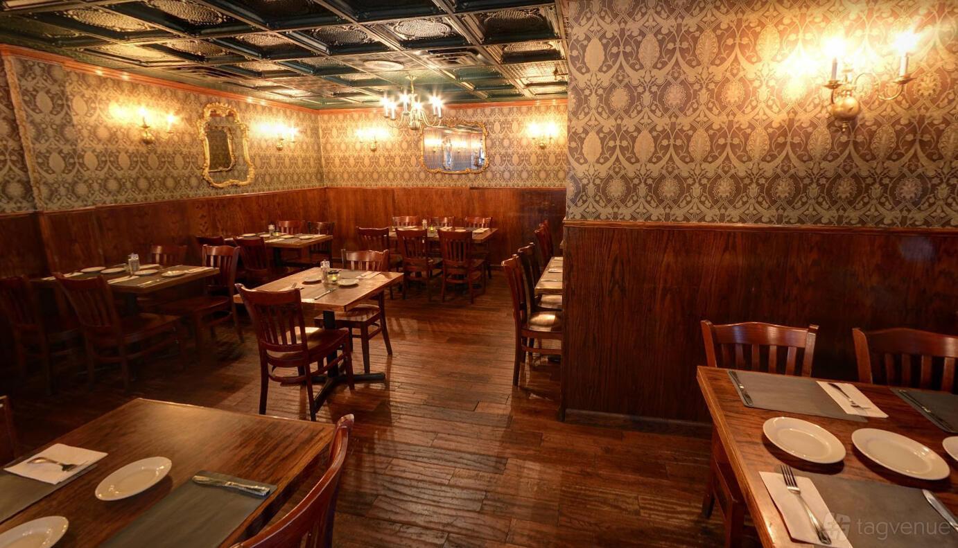 A restaurant dining room with wooden floors, patterned wallpaper, chandeliers, and wooden tables at West Shore Inn.