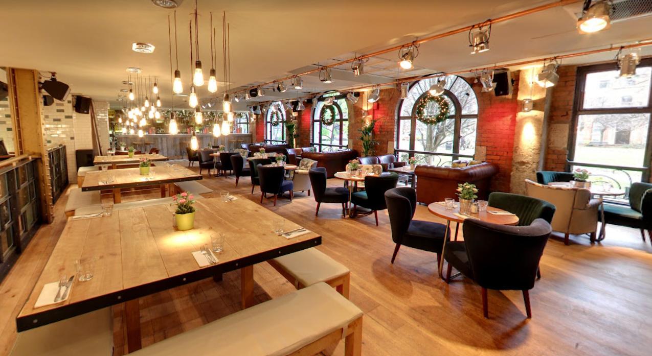 An event space in a bar with exposed brick arches, large windows, and wooden tables at Revolution Parsonage Gardens.