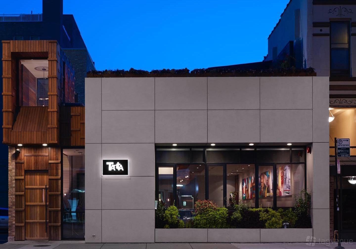 A restaurant with a modern exterior, large front windows, and a lit sign at Tanta Chicago.