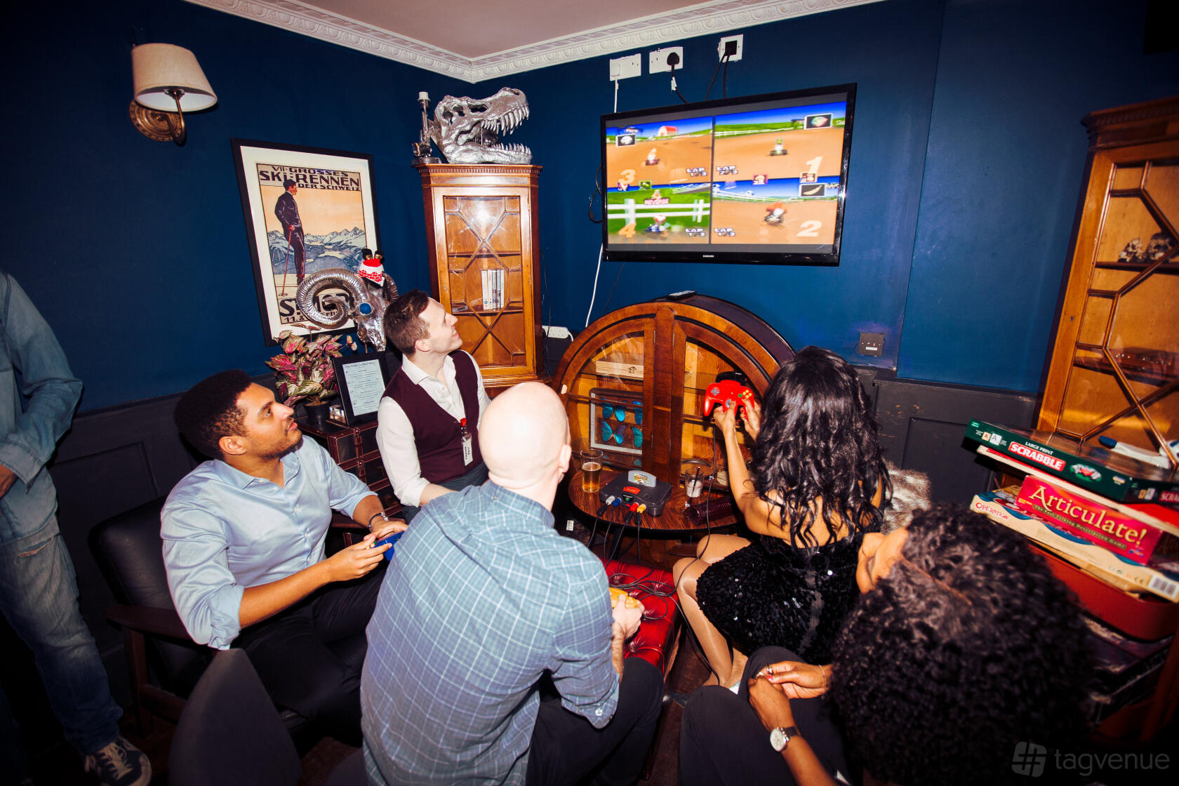 An event space in a cocktail bar with navy walls, vintage decor, and people playing video games at The Little Blue Door.