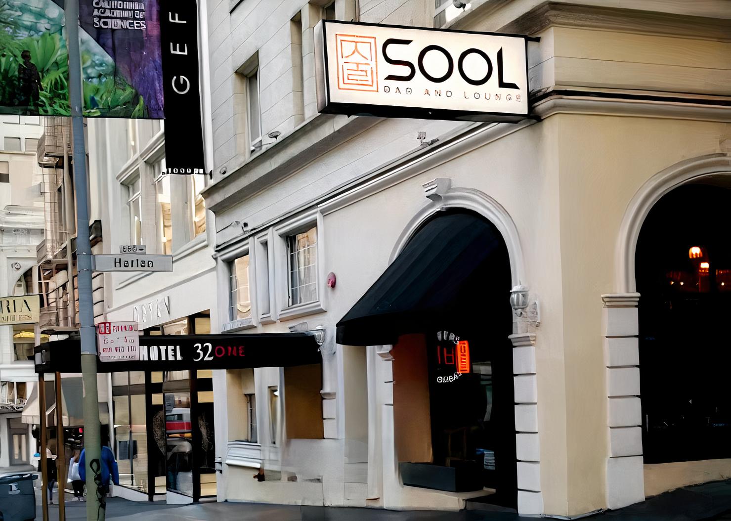 A pub and bar with an illuminated sign above an arched entrance on a city street at Sool Bar and Lounge.