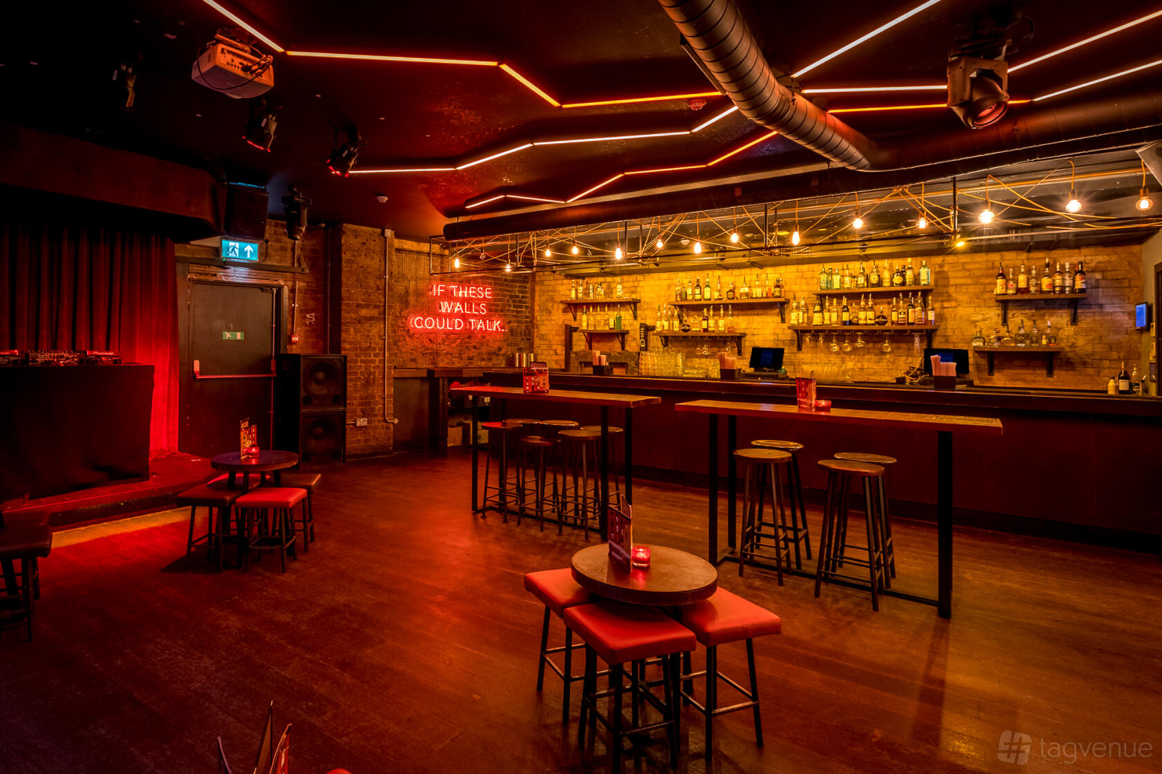A basement bar with exposed brick walls, neon signage, a backlit bar, and high tables at Old Street Records.