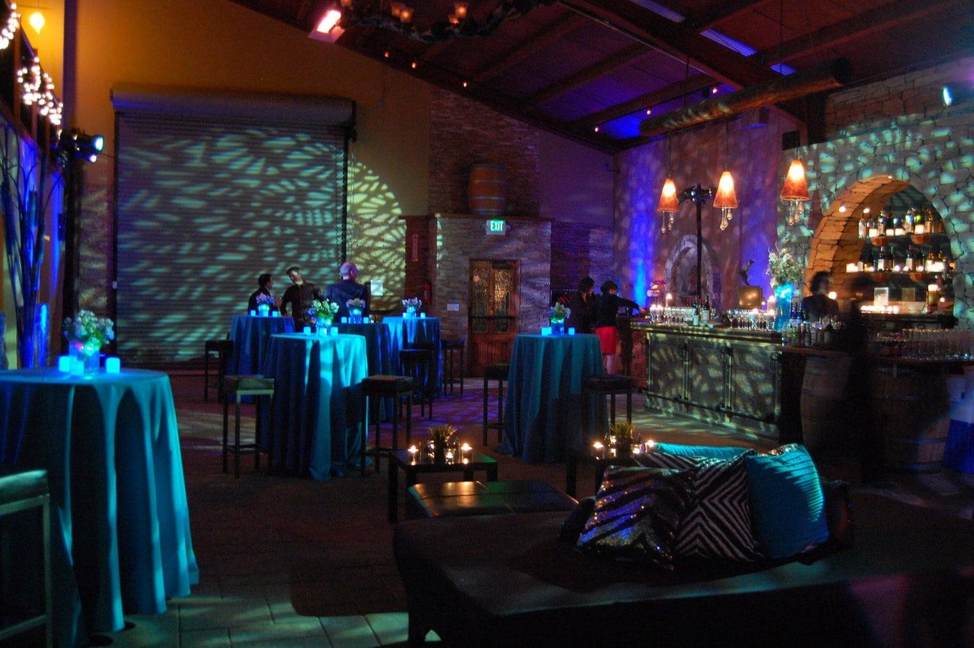An event venue with dramatic blue lighting, high ceilings, cocktail tables, and stone walls at La Honda Winery.