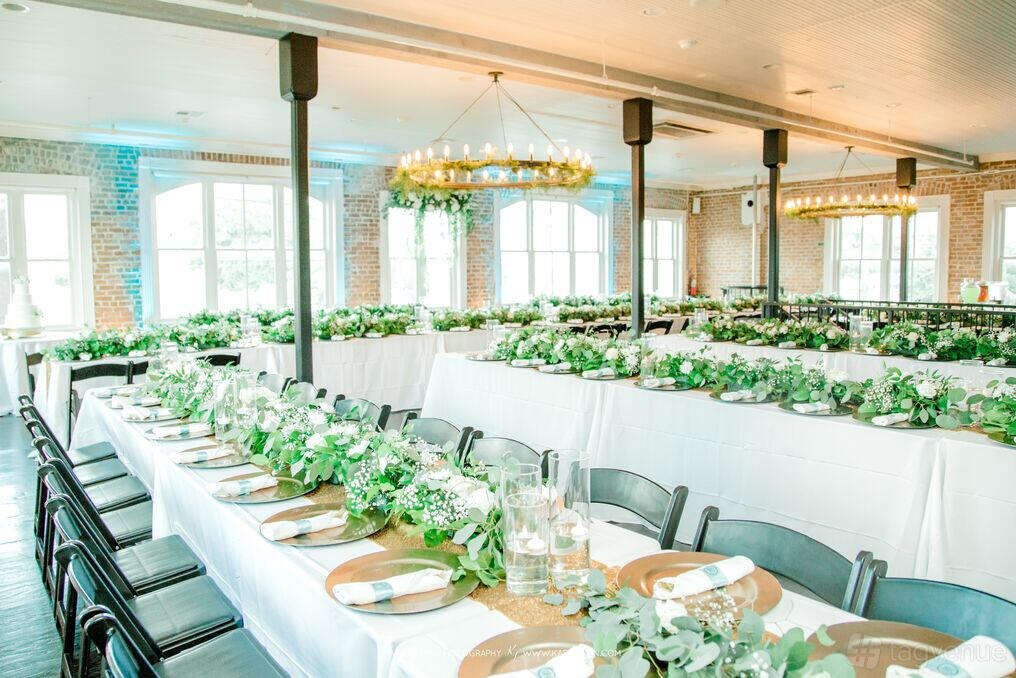 An event venue with long banquet tables decorated with greenery and large windows at Station 3.
