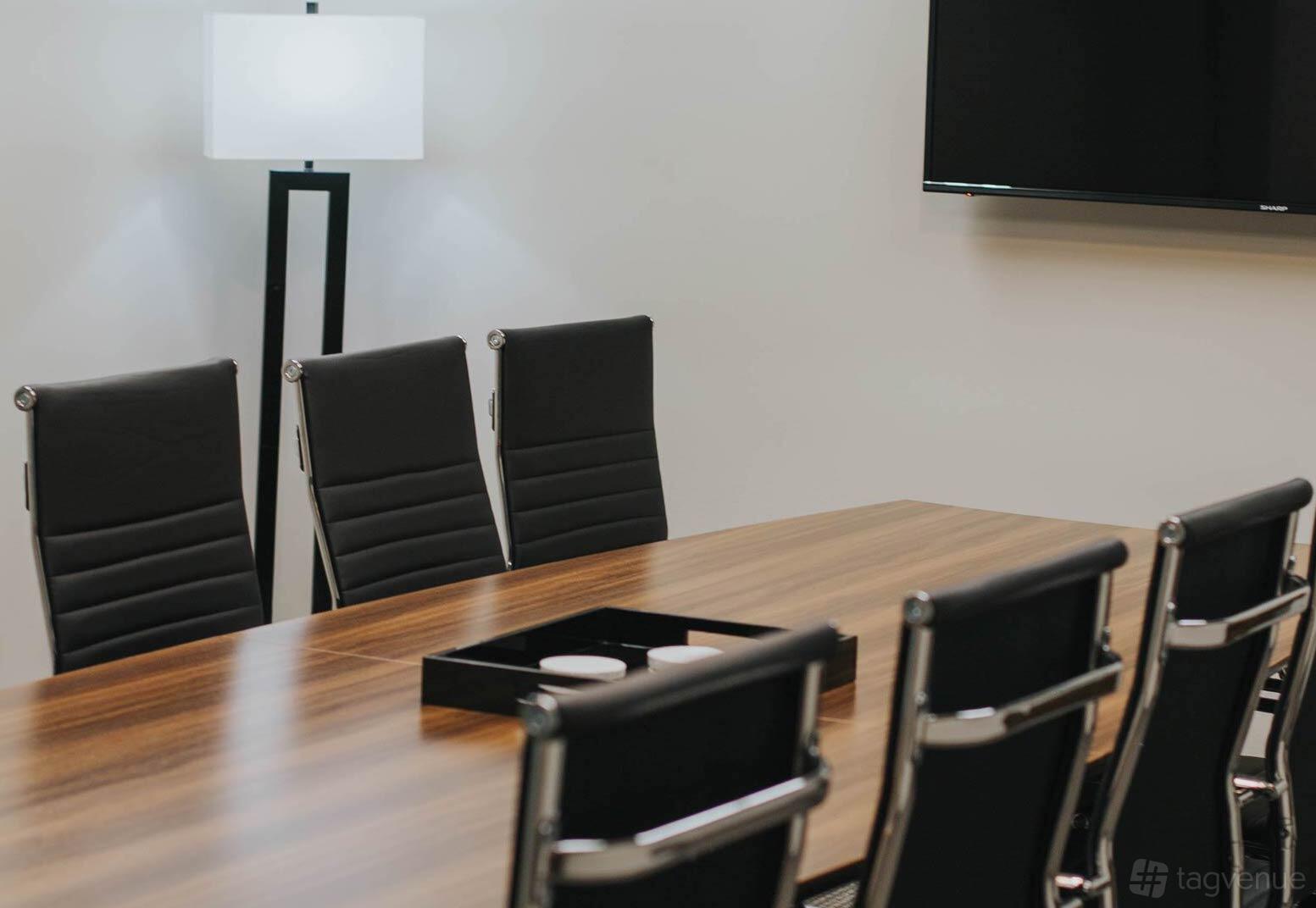 A meeting room with black leather chairs, a wood conference table, and a wall-mounted TV at Executive Workspace Uptown Dallas.