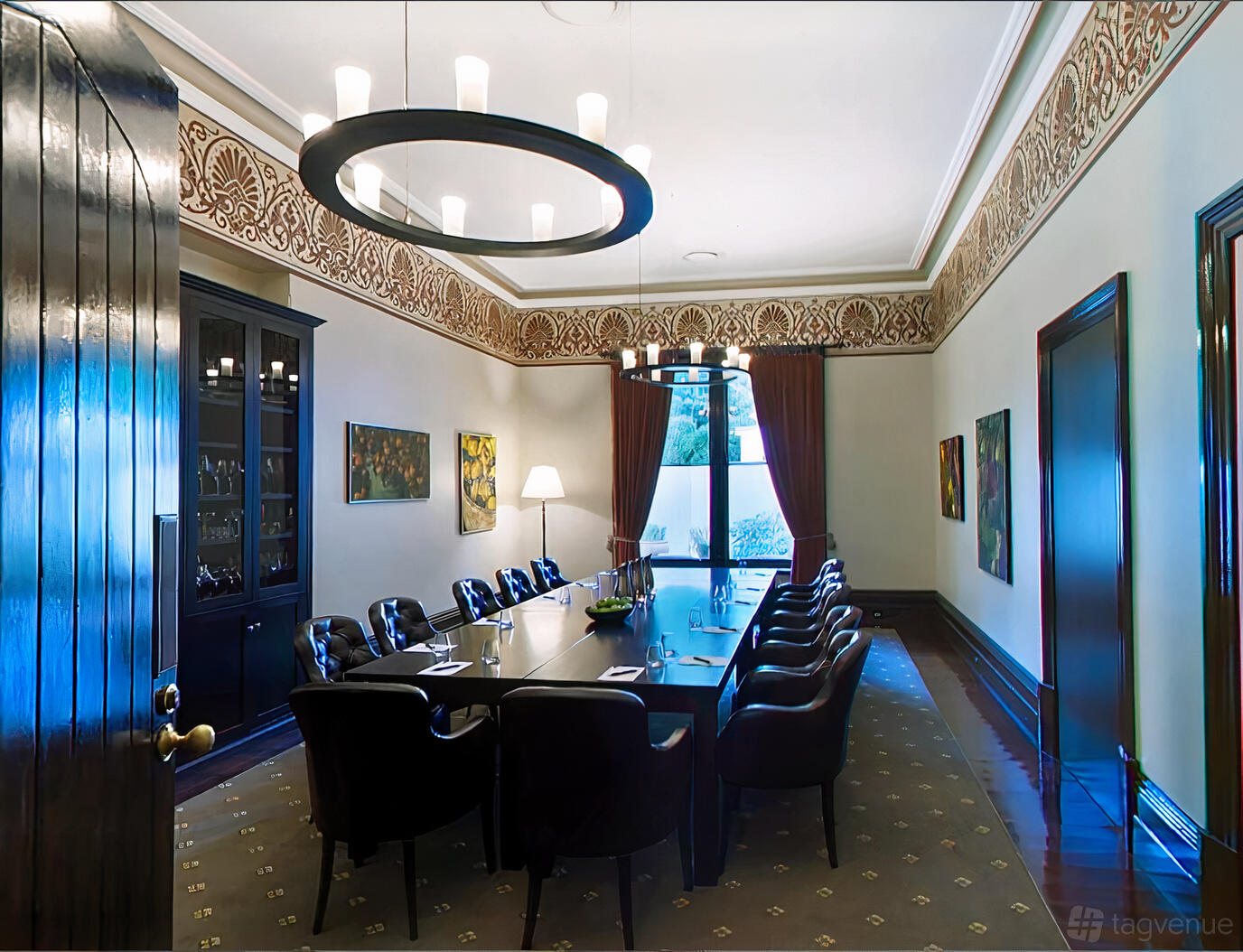 A dining room with a long dark wood table, leather chairs, artwork on the walls, and tall windows at Mount Lofty House and Estate.