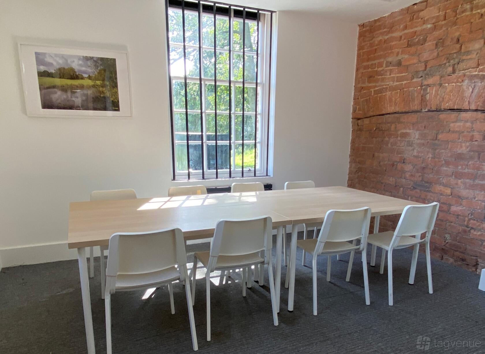 A meeting room with a light wood table, white chairs, exposed brick wall, and barred window at Bowring Park and Golf Course.