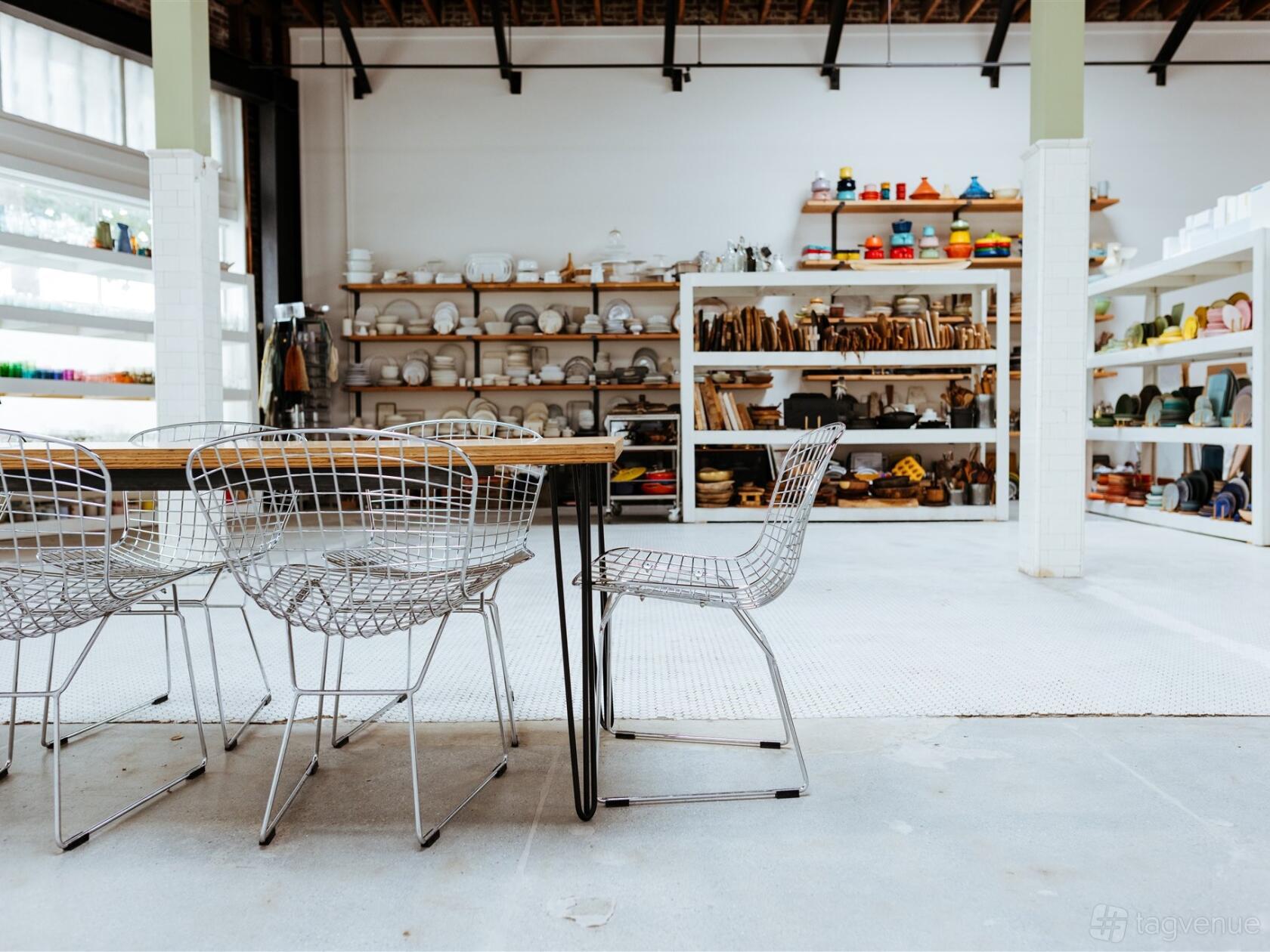 A photo studio with a long wooden table, wire chairs, and open shelving filled with ceramics at Cosita.