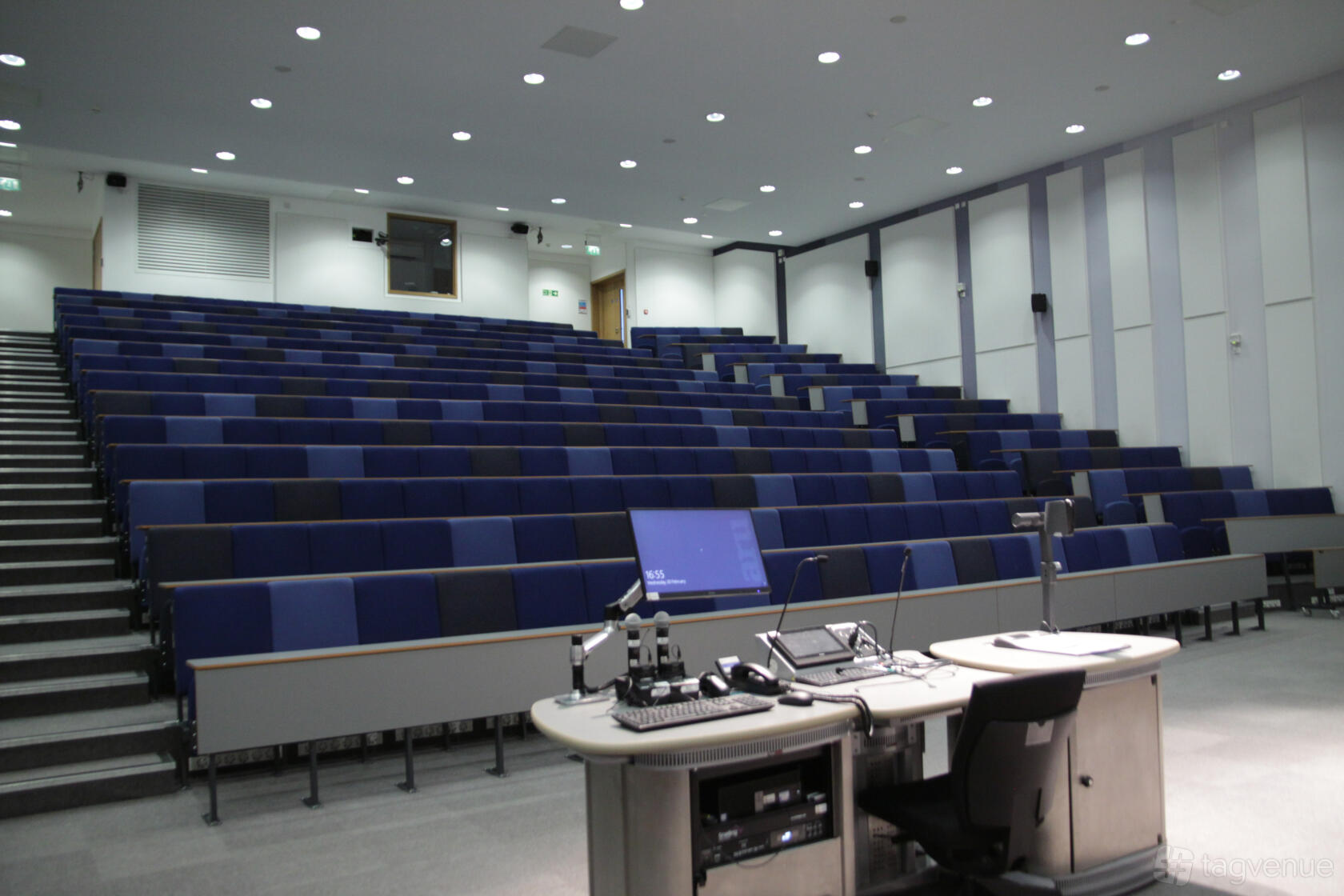 An auditorium with tiered rows of blue seats and a lectern equipped with AV controls at ARU Venue Hire - Chelmsford.