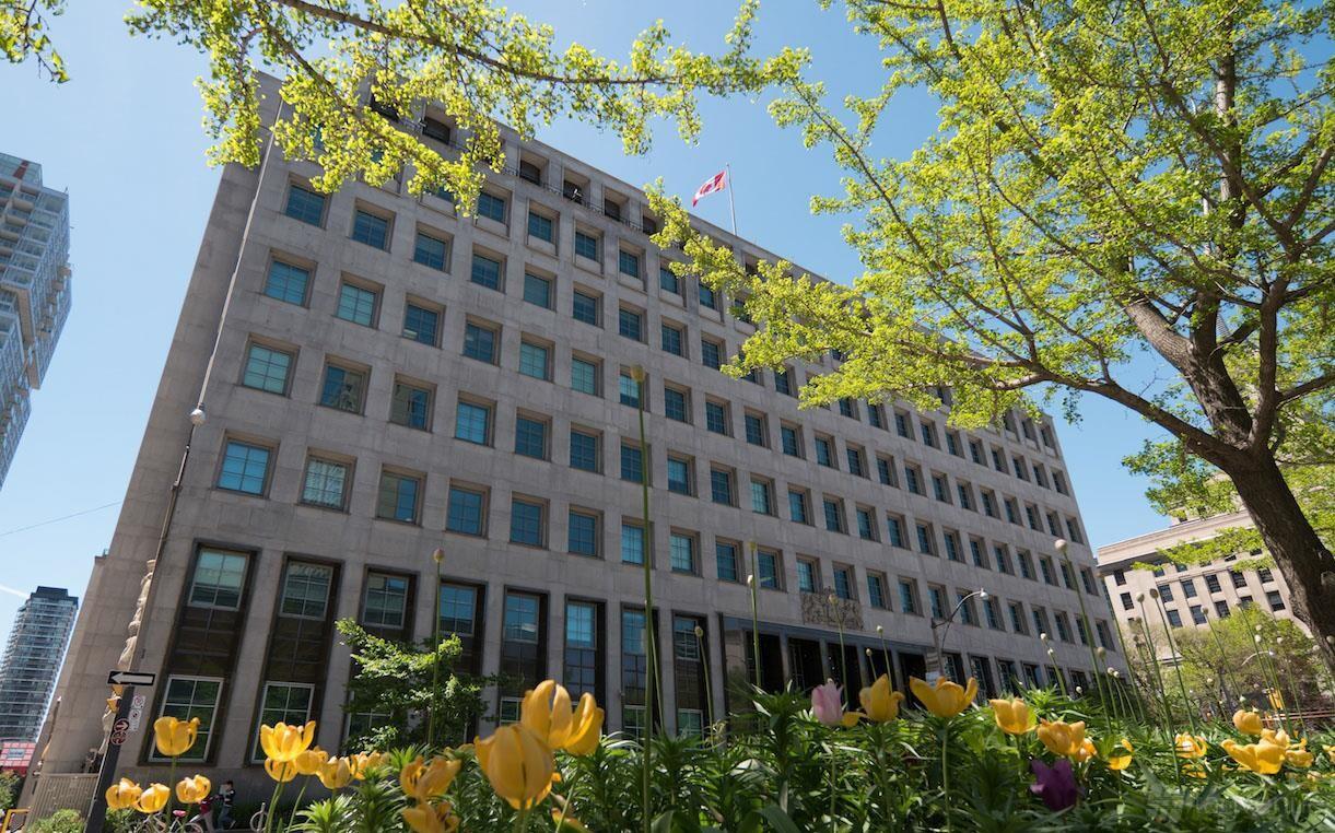 A historic building with a stone facade, rows of large windows, and blooming tulips at iQ Offices - 250 University Avenue.