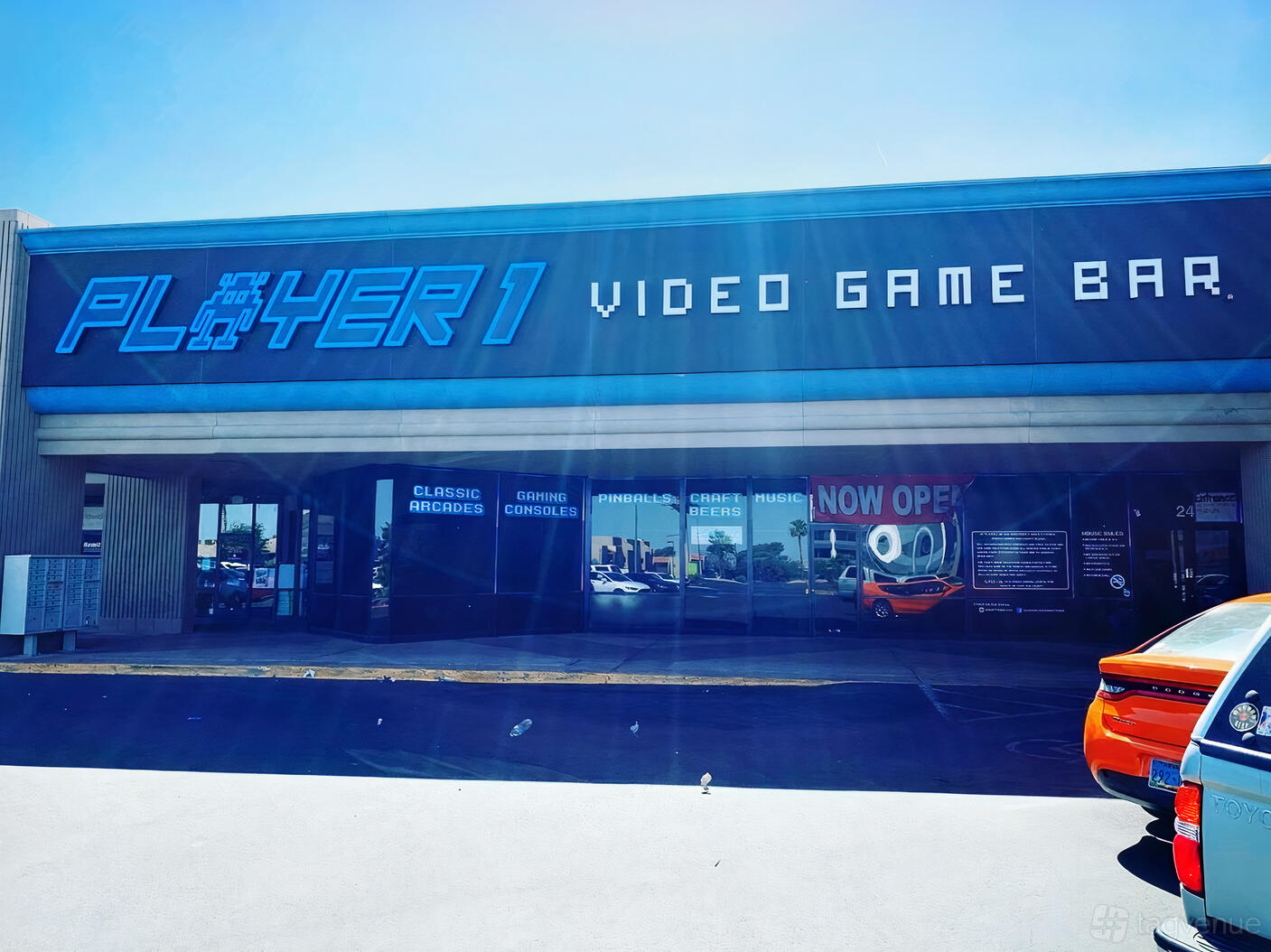 An exterior view of a bar with a blue neon sign and large front windows at Player 1 Video Game Bar - Las Vegas.