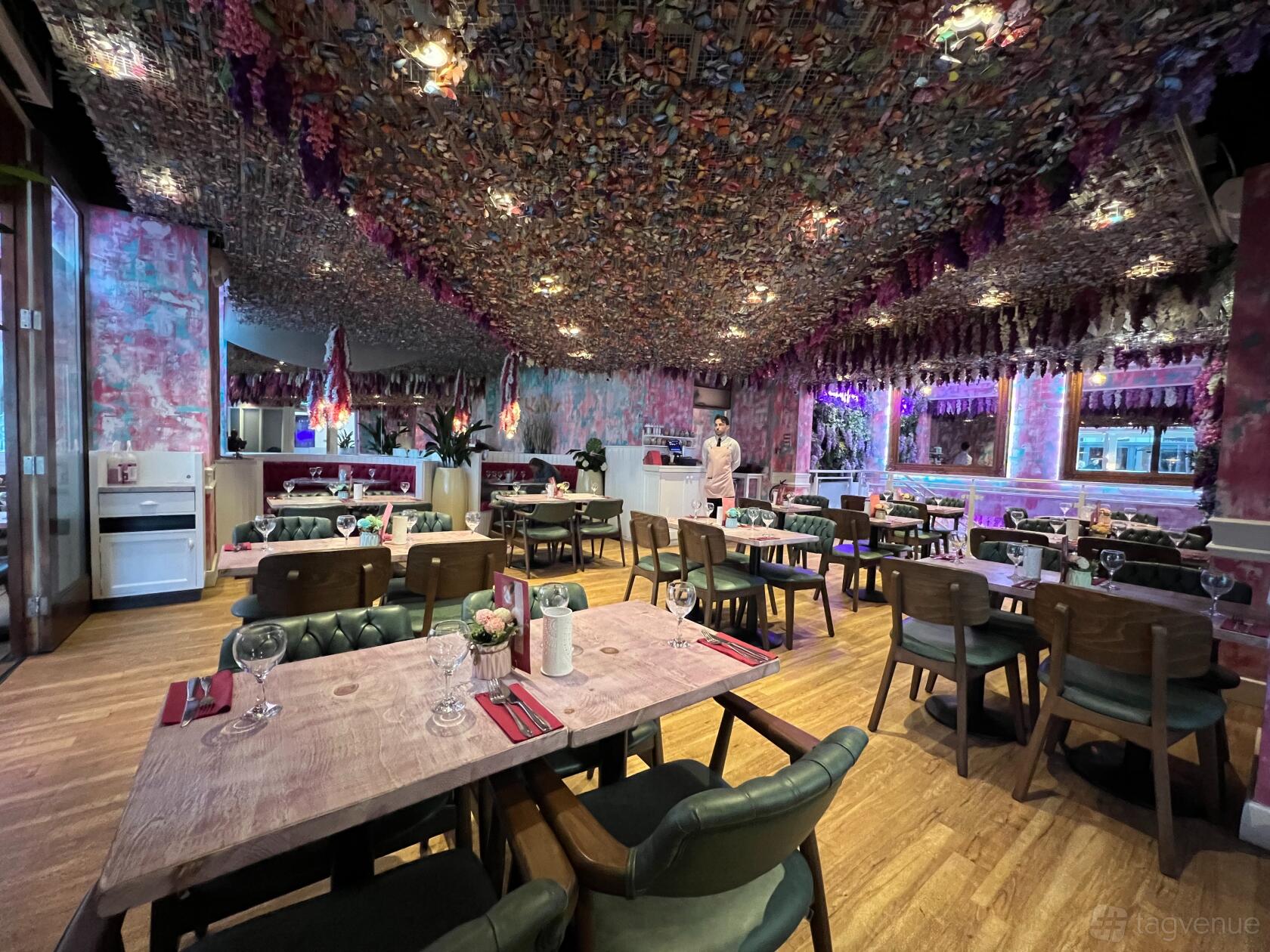 A restaurant with floral ceiling decor, wooden tables set with glassware, and large windows at Fleur Restaurant & Bar Leeds city Centre.