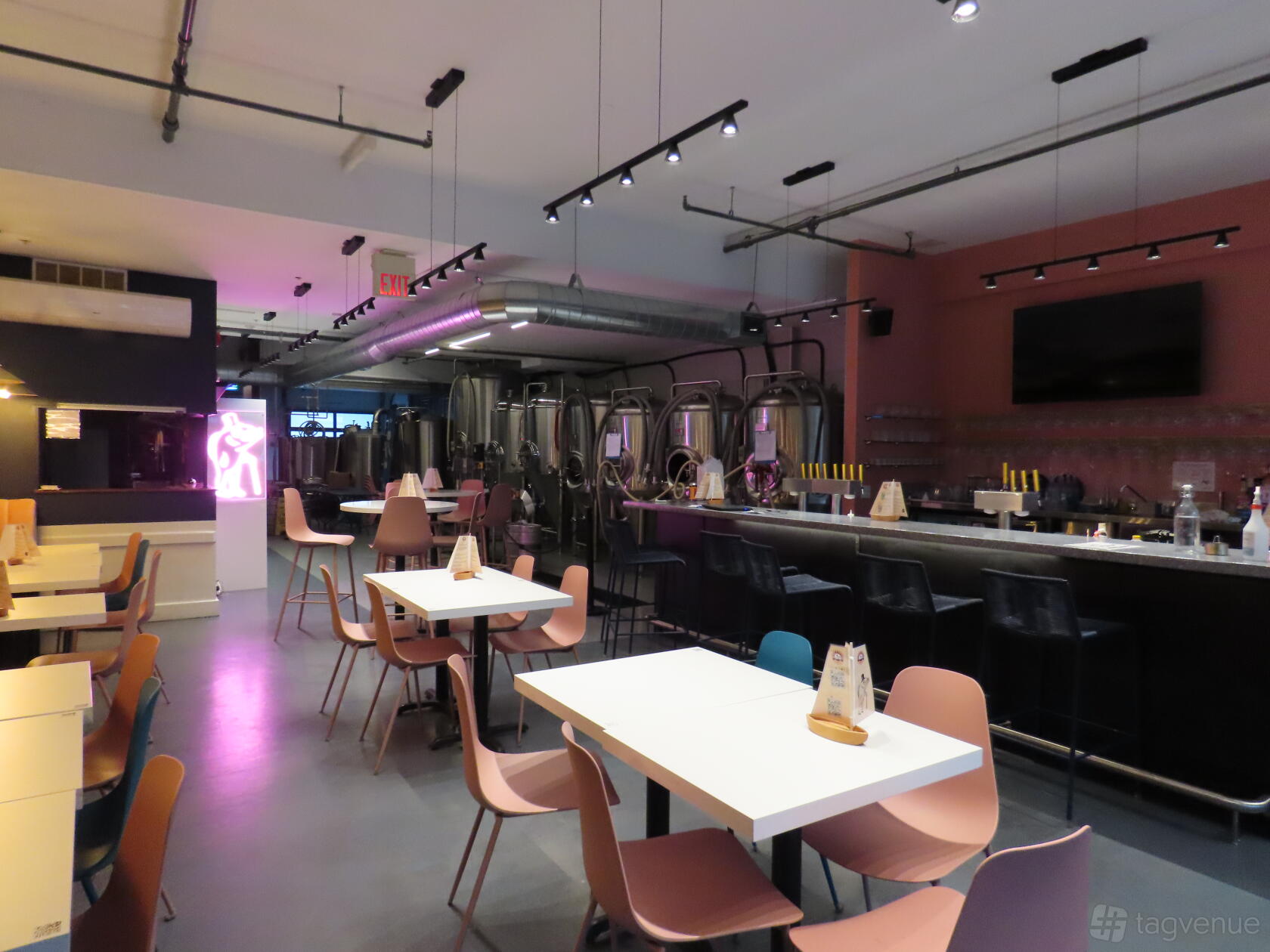 A brewery with stainless steel brewing tanks behind a long bar and pastel chairs at Something in the Water Kingston.