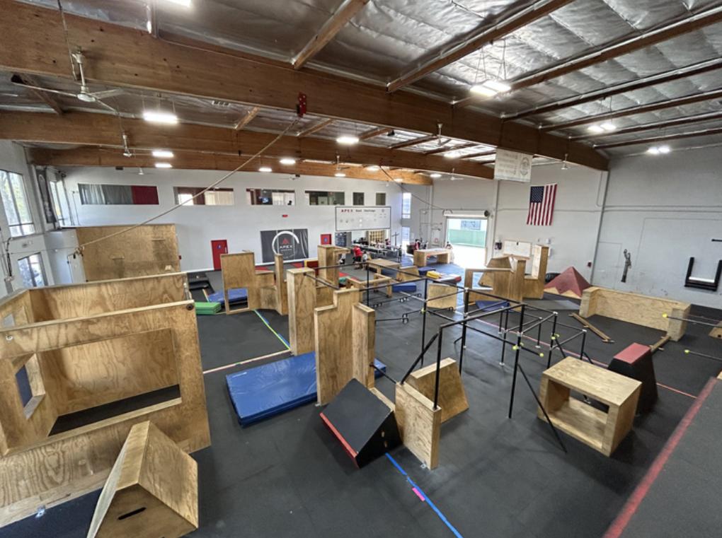 An event space with parkour obstacles, wooden platforms, mats, and metal bars at APEX School of Movement San Diego.