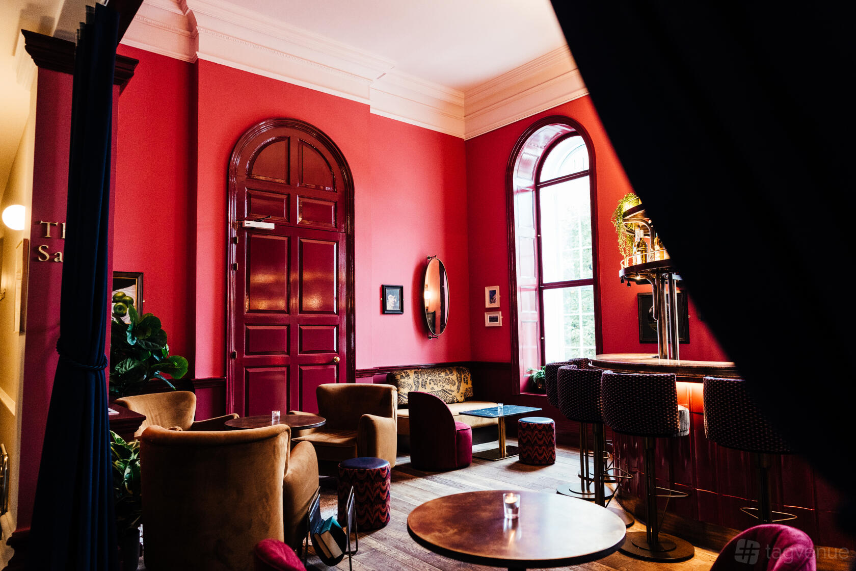 An event venue with high ceilings, red walls, arched windows, and velvet lounge seating at Kindred.