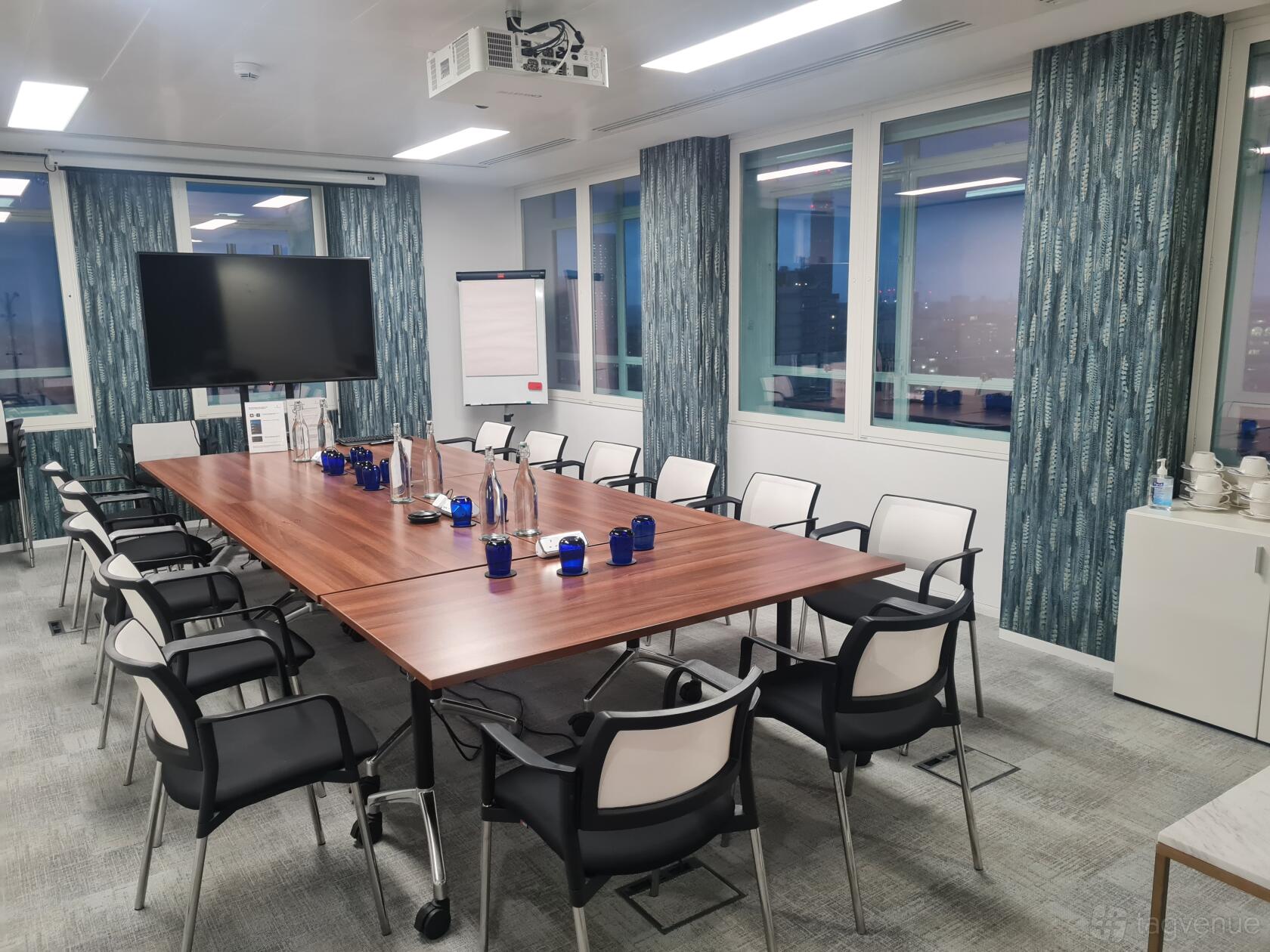 A meeting room with a large wooden conference table, wall-mounted screen, and windows at Landmark: Cavendish Square, London.