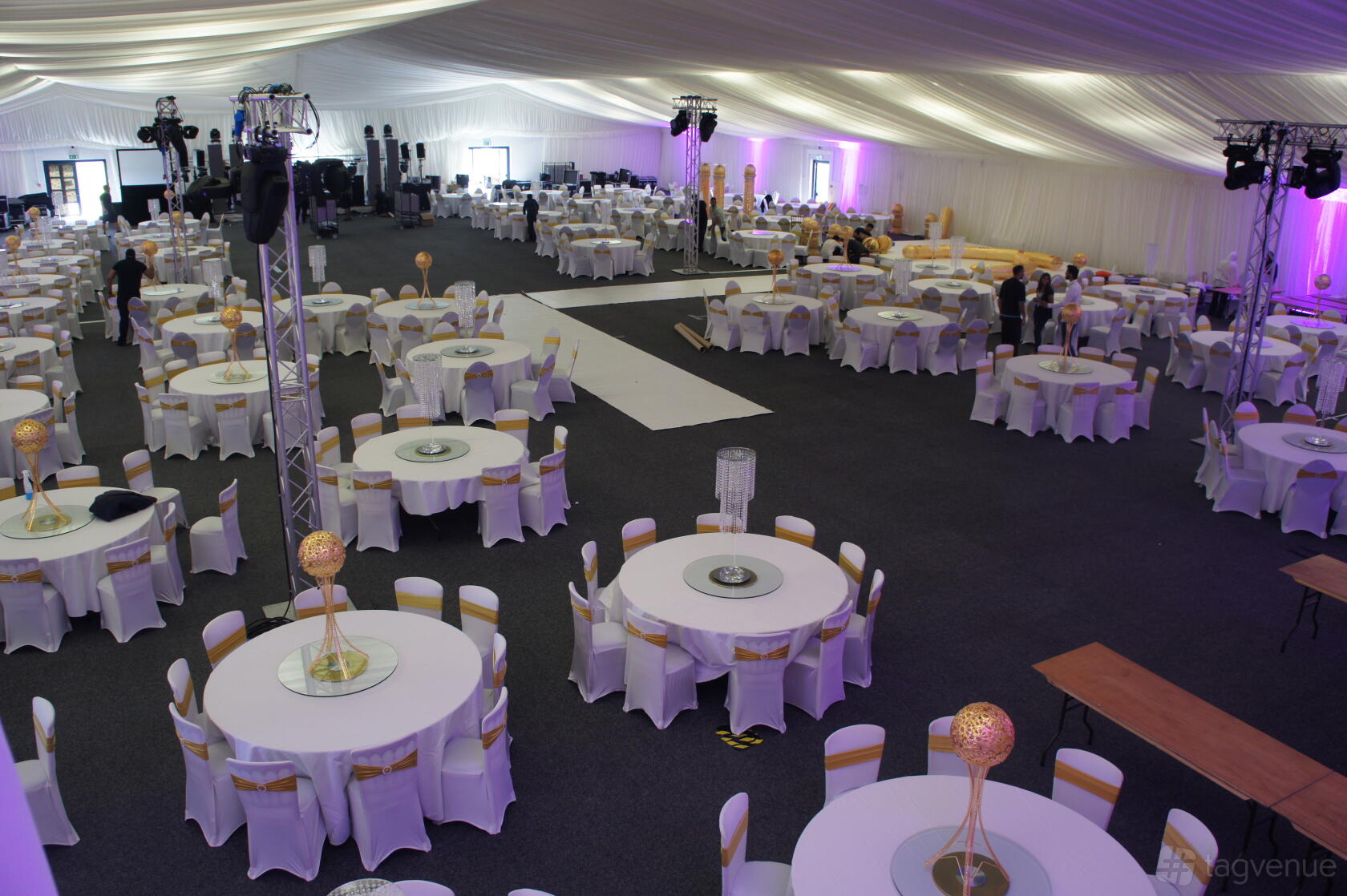A spacious hall with round tables dressed in white linens and gold accents under a draped ceiling at Kent Event Centre.