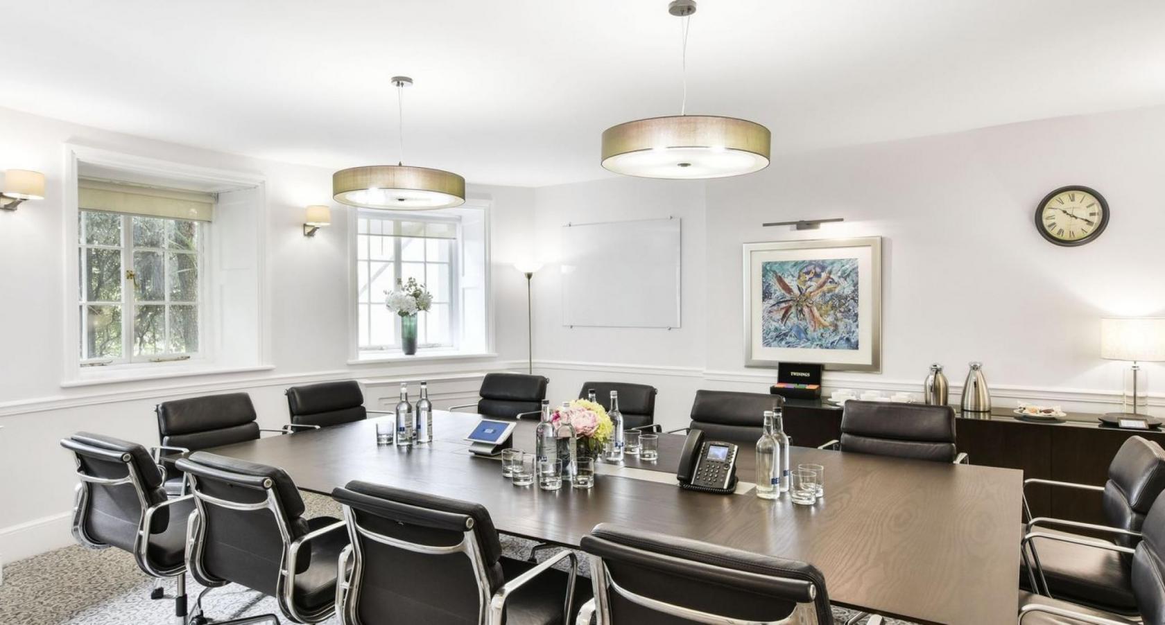 A meeting room with a long conference table, black leather chairs, wall art, and large windows at 32 Curzon Street.