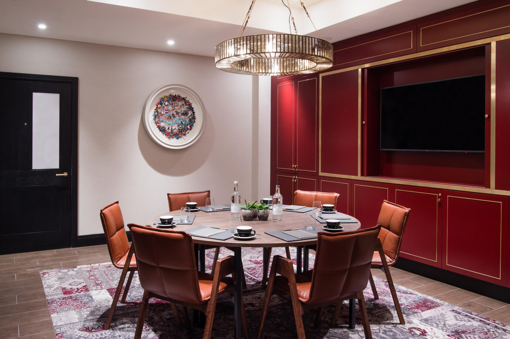 A meeting room with a round table, leather chairs, a wall-mounted TV, and red-paneled cabinetry at Vintry & Mercer.