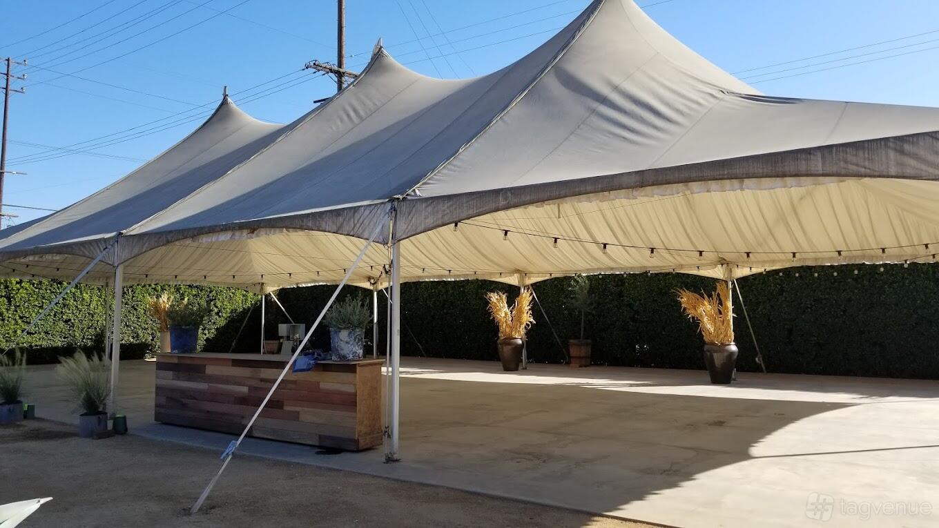 An outdoor event venue with a large white tent, string lights, and potted plants at Rolling Greens On Mateo.